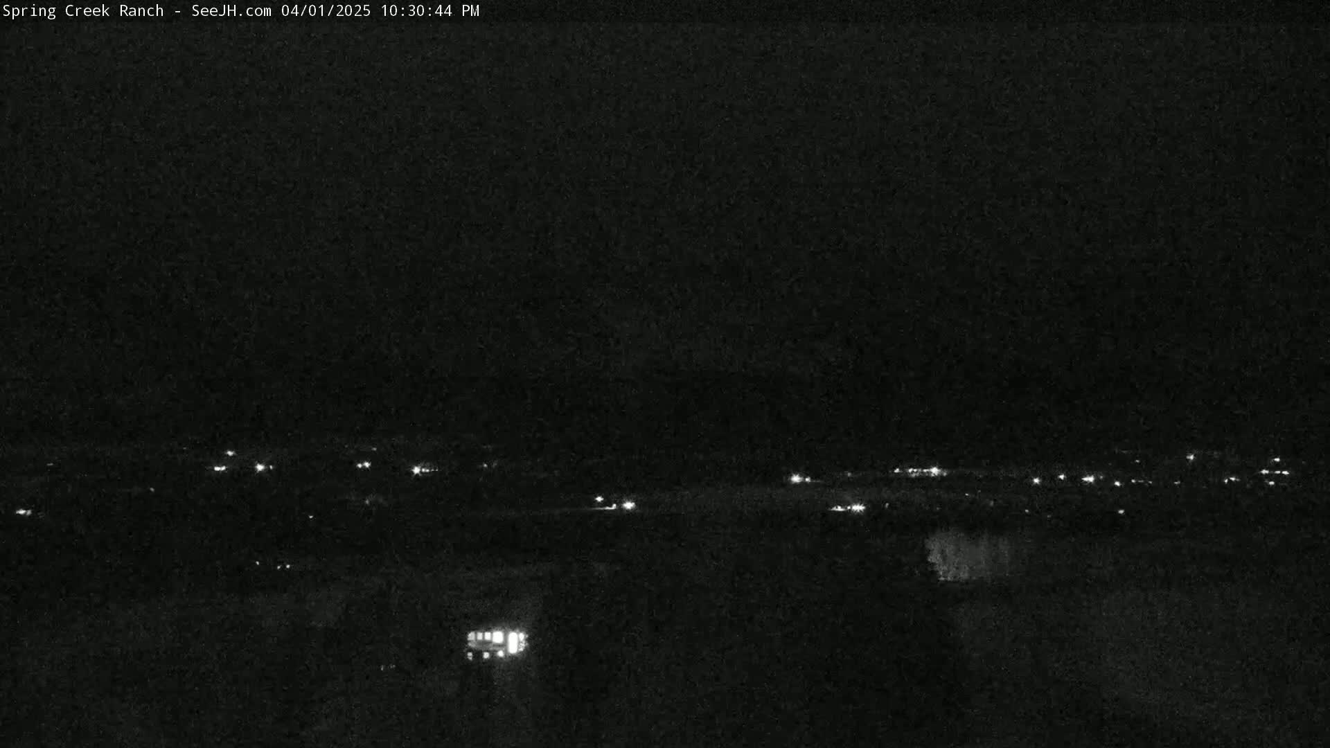 A nighttime, long-range view shows a distant line of lights, possibly from a town or road, under a dark, clear sky.