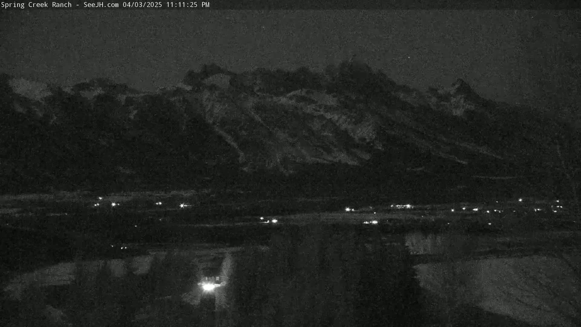 A nighttime long shot shows a mountain range under a dark sky, with a few small lights visible in the valley below.