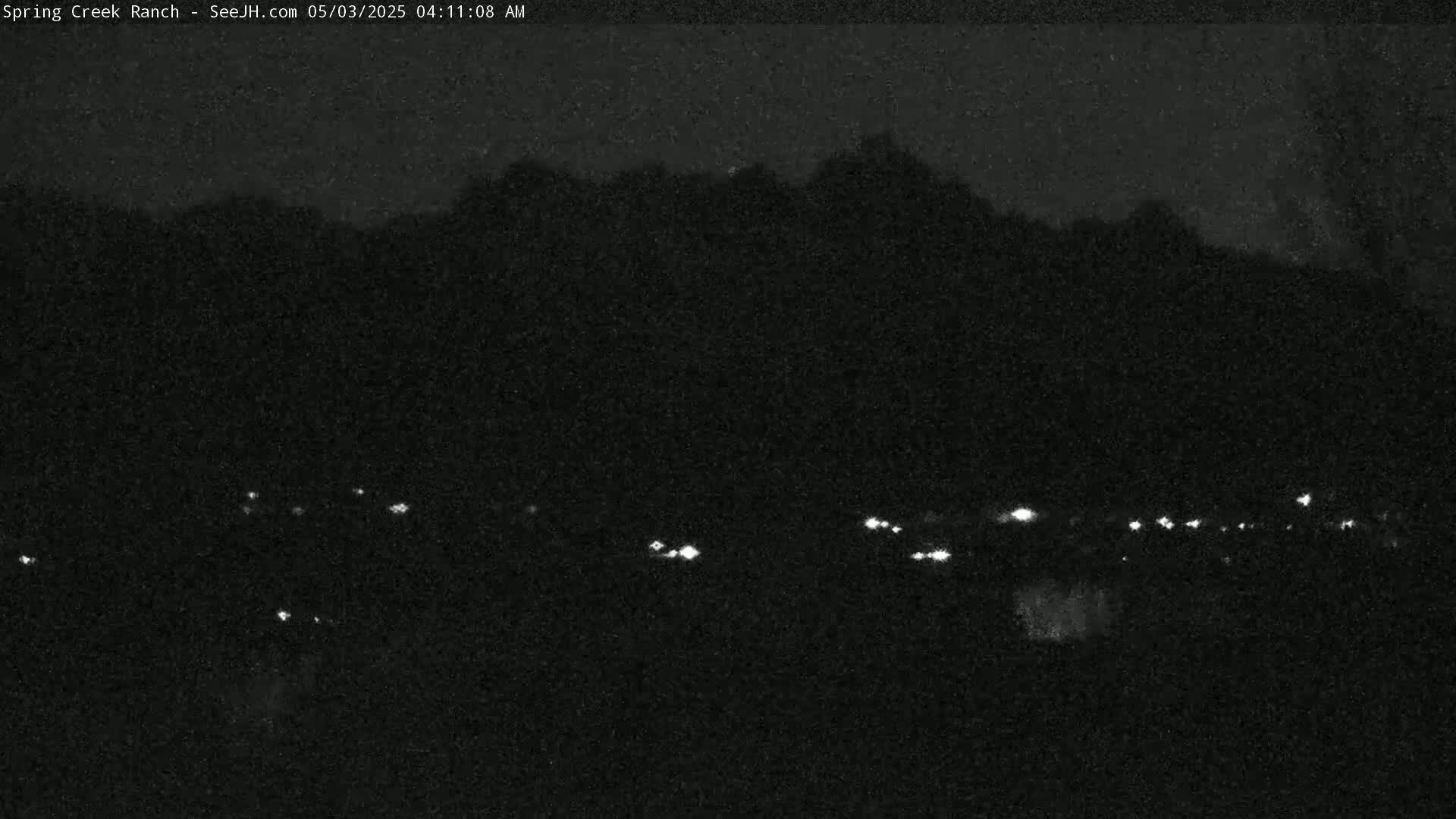 A nighttime view shows a dark, silhouetted hillside with a scattering of small, distant lights below it.