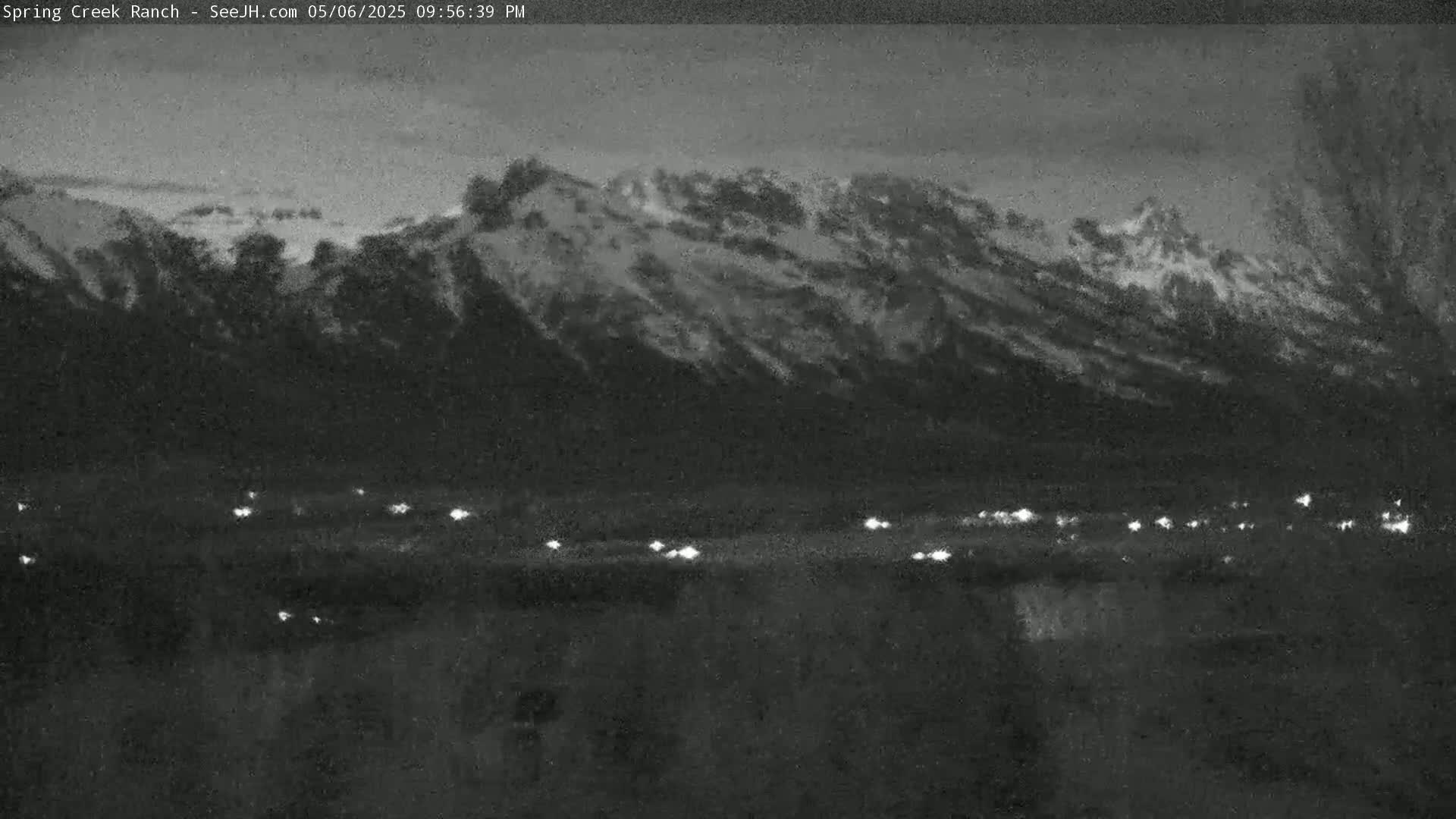 A nighttime, low-light view shows snow-covered mountains in the background, with a line of small, distant lights in the foreground.