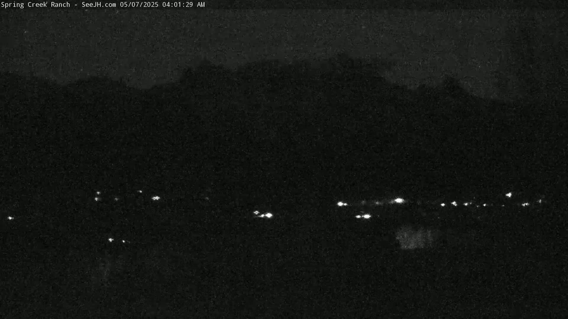 A nighttime long shot shows a dark landscape with a line of distant lights under a dark, overcast sky.