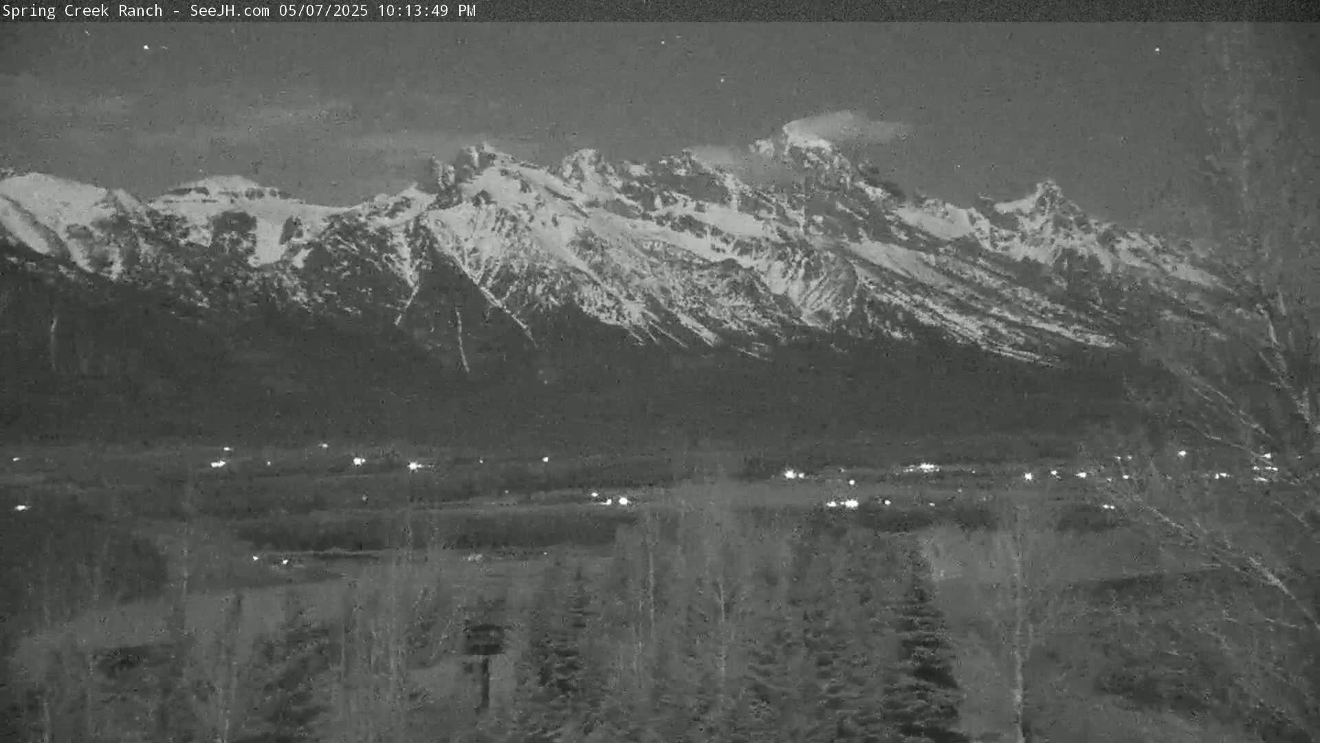 A snow-capped mountain range is visible at night, with a few scattered lights illuminating a valley in the foreground.
