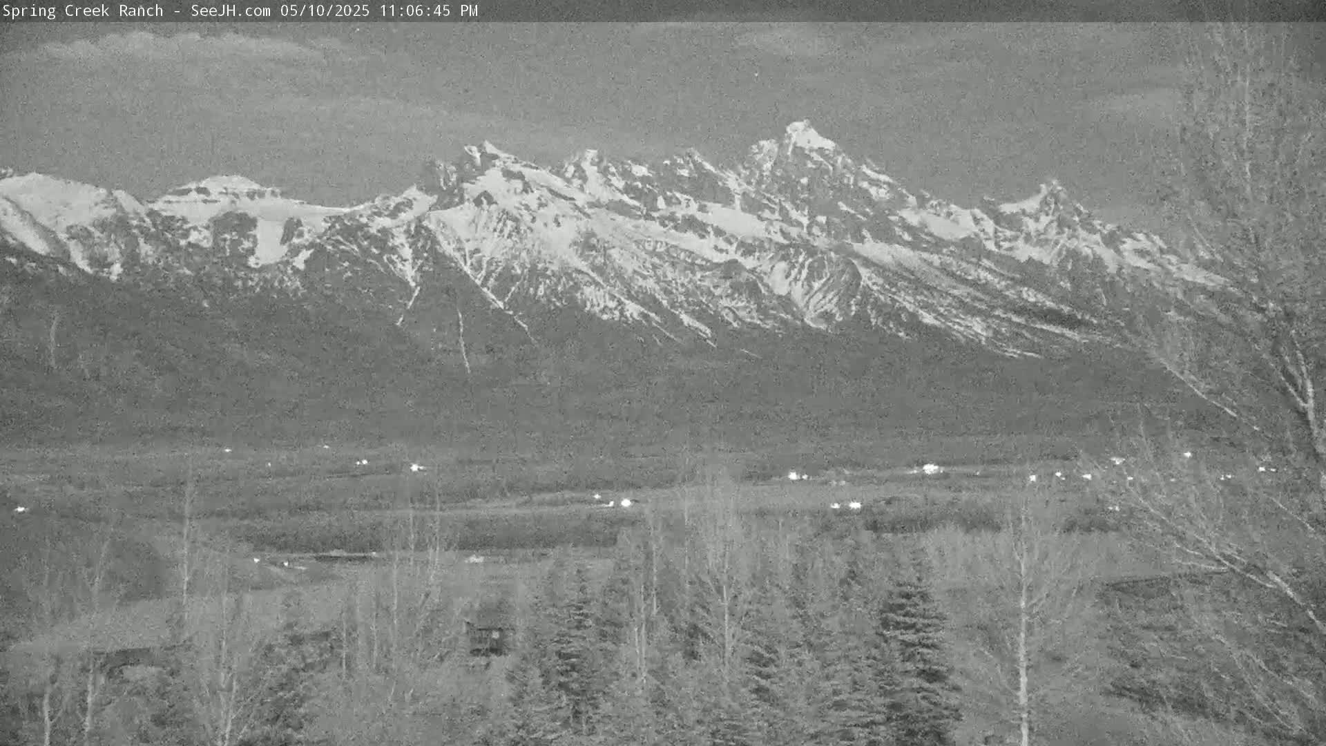 A snow-capped mountain range is visible at dusk, with a flat valley and sparse trees in the foreground.