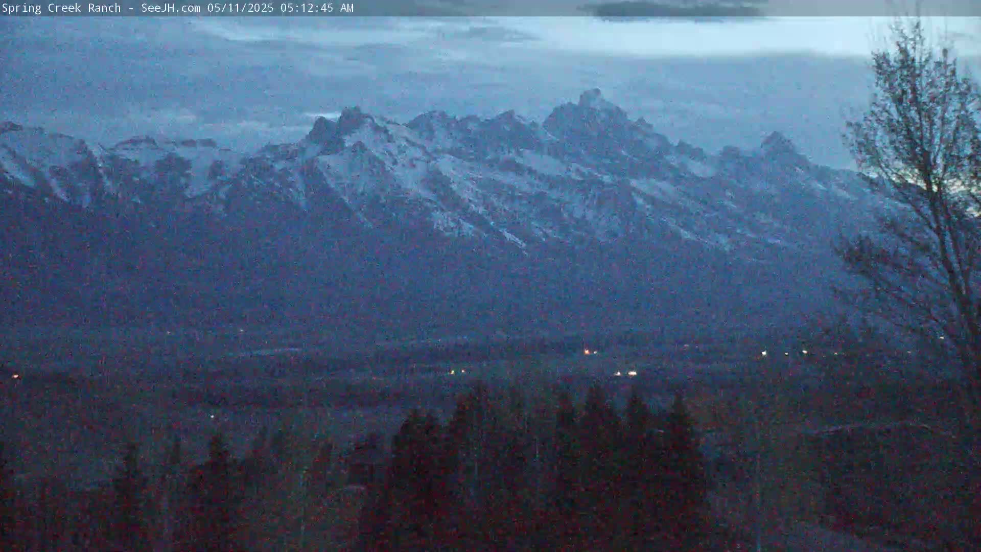 Snow-capped mountains are visible at dusk, with a valley and dark trees in the foreground.