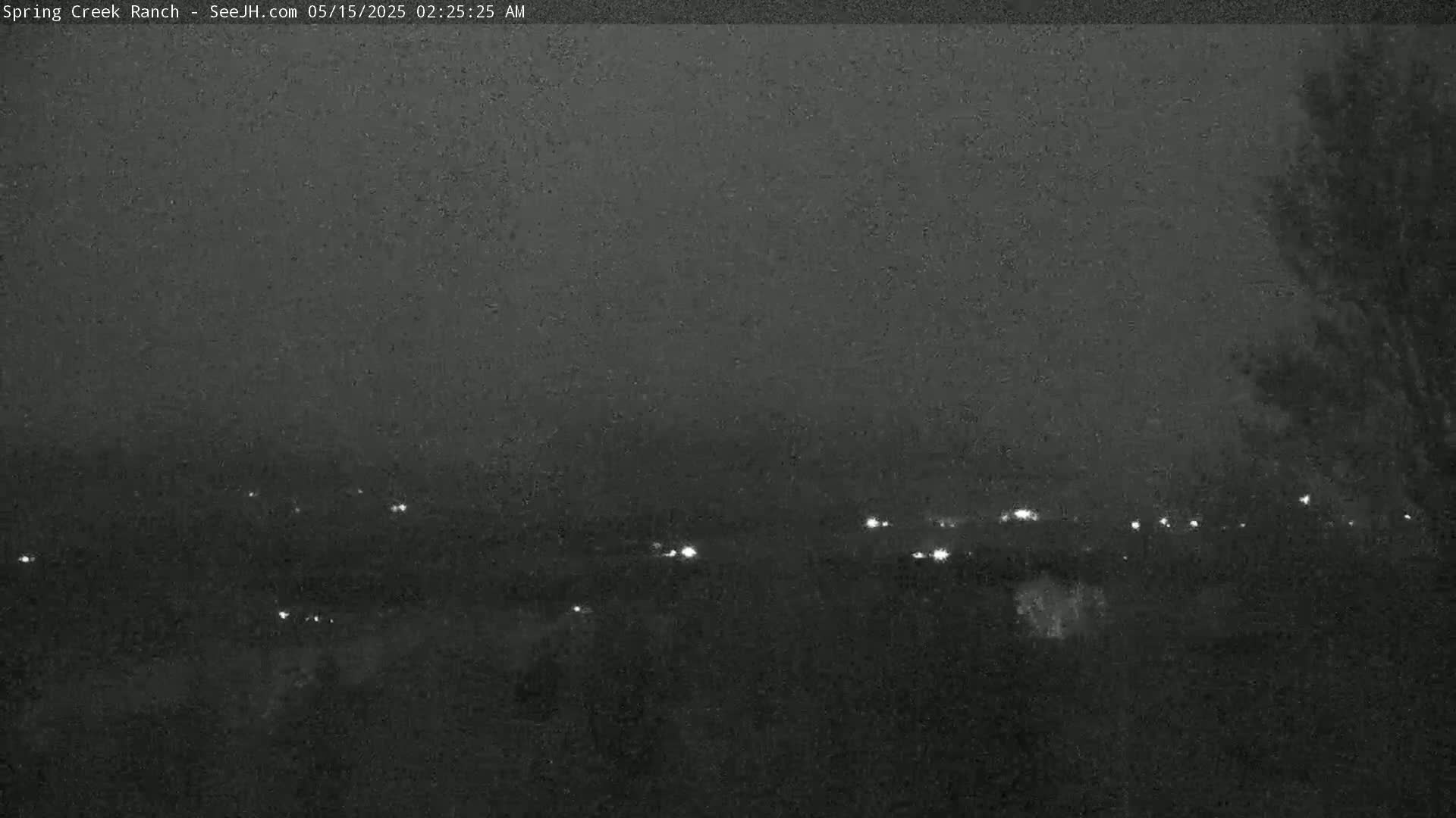 A nighttime, low-light view of a distant landscape with faint lights scattered across the horizon under a possibly snowy or hazy sky.