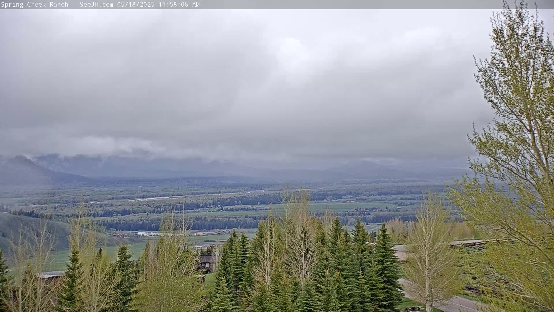 A cloudy, overcast view shows a vast valley with green trees and fields, extending to distant mountains partially obscured by low clouds.