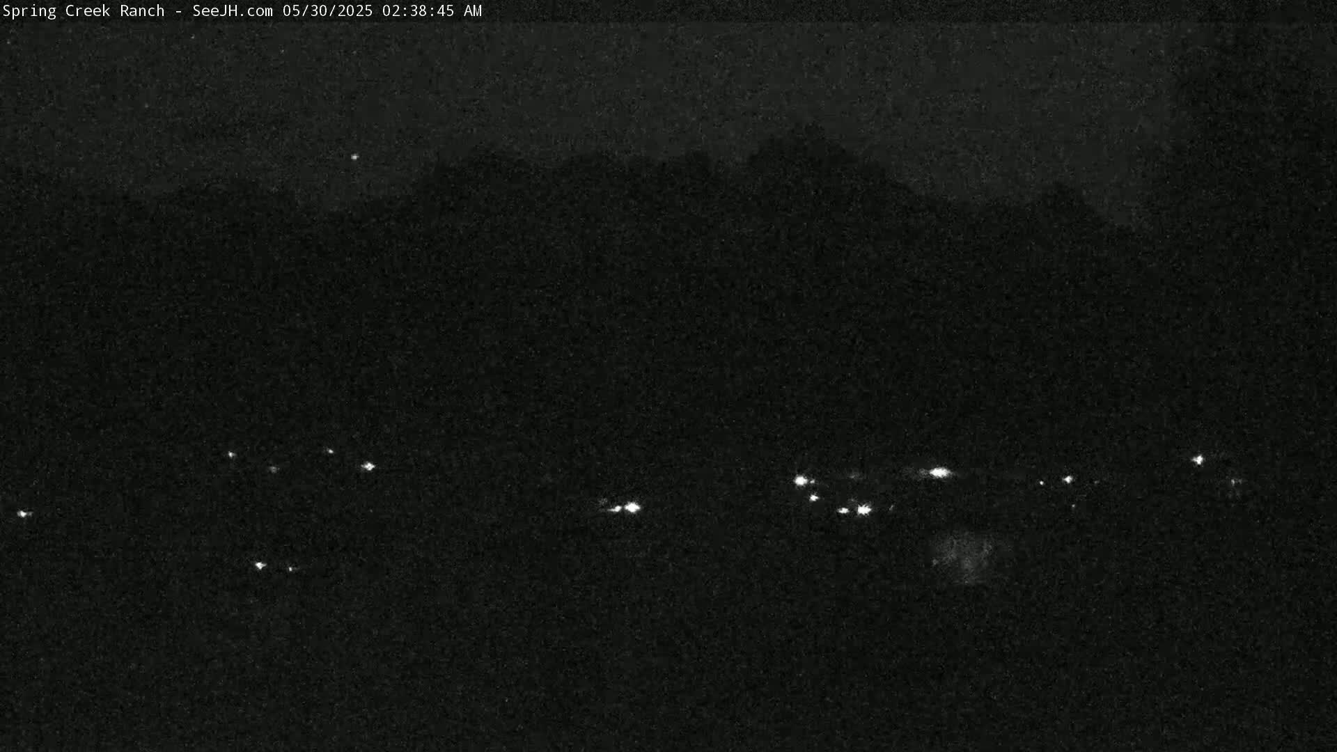A nighttime, low-light image shows a dark landscape with a few small, distant lights visible.