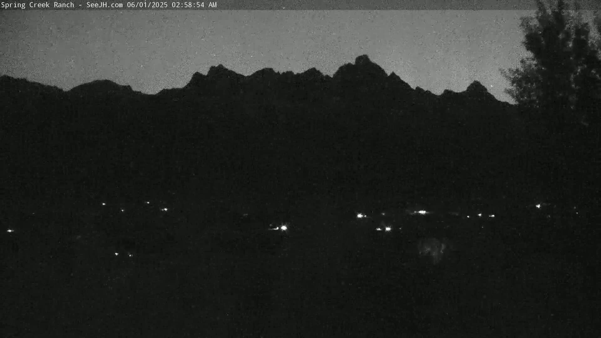 A nighttime view shows a dark mountain range silhouetted against a twilight sky, with a few faint lights visible in the foreground.