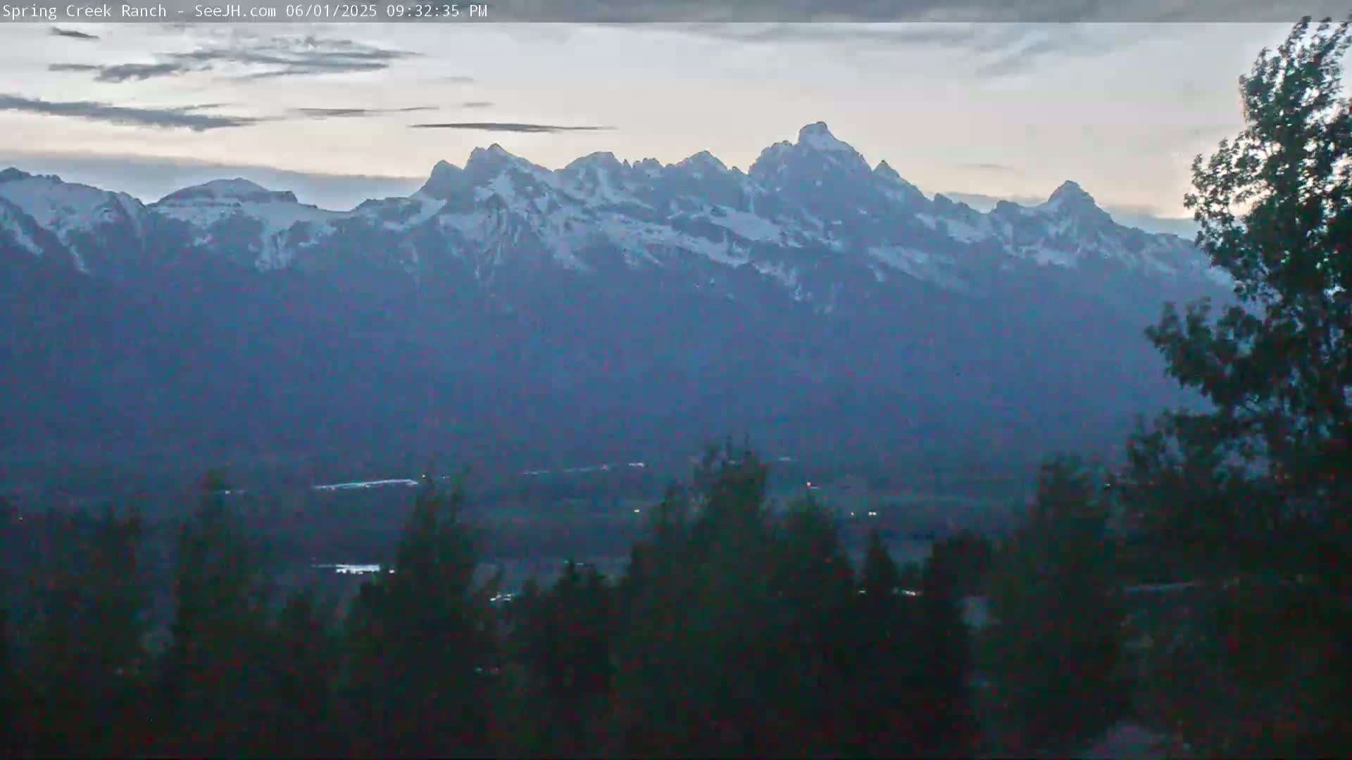Snow-capped mountains are visible in the distance under a cloudy, twilight sky, with dark trees in the foreground.