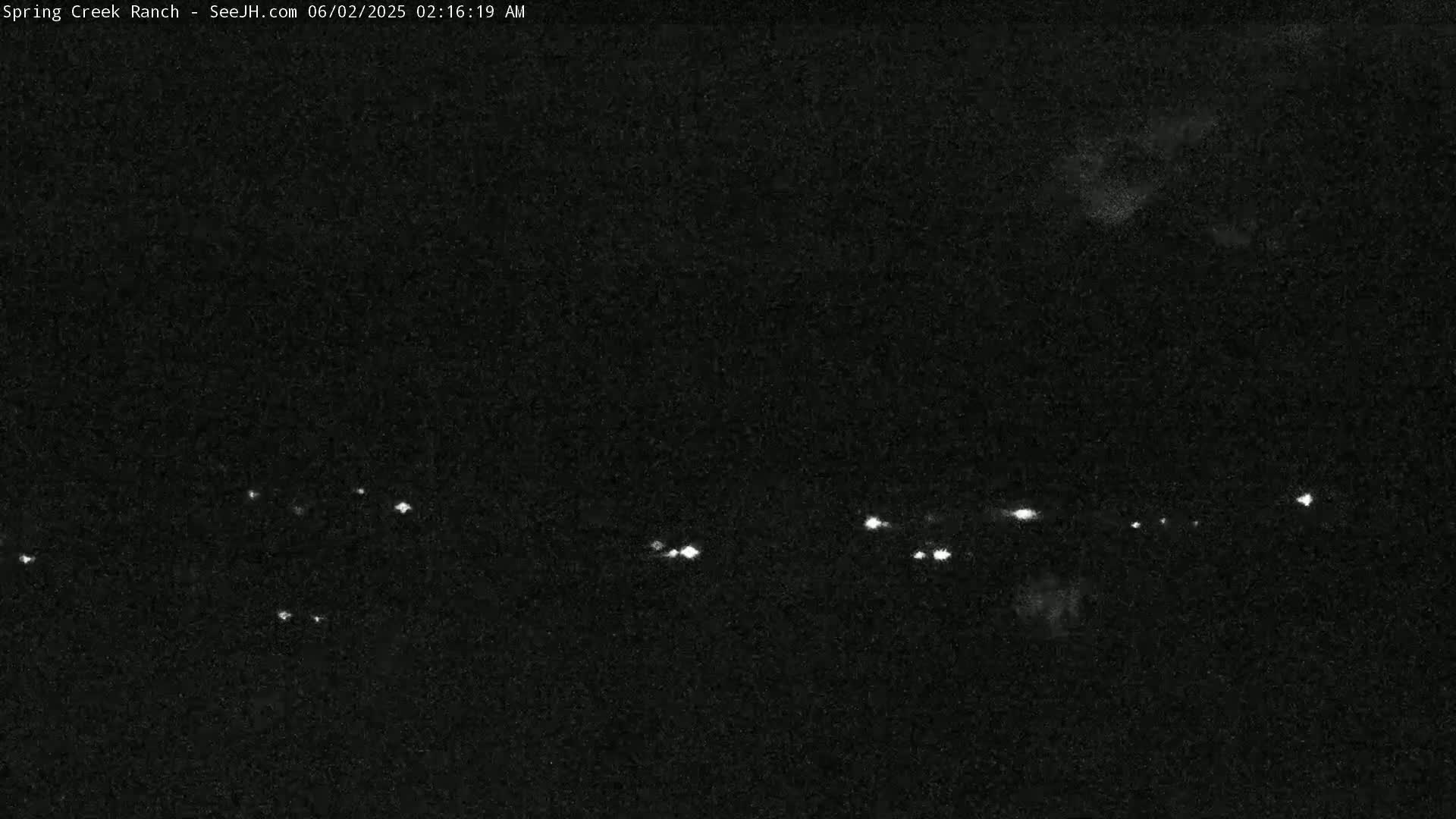 A nighttime, low-light image shows a scattering of faint lights in the distance, possibly vehicle headlights, under a dark sky.
