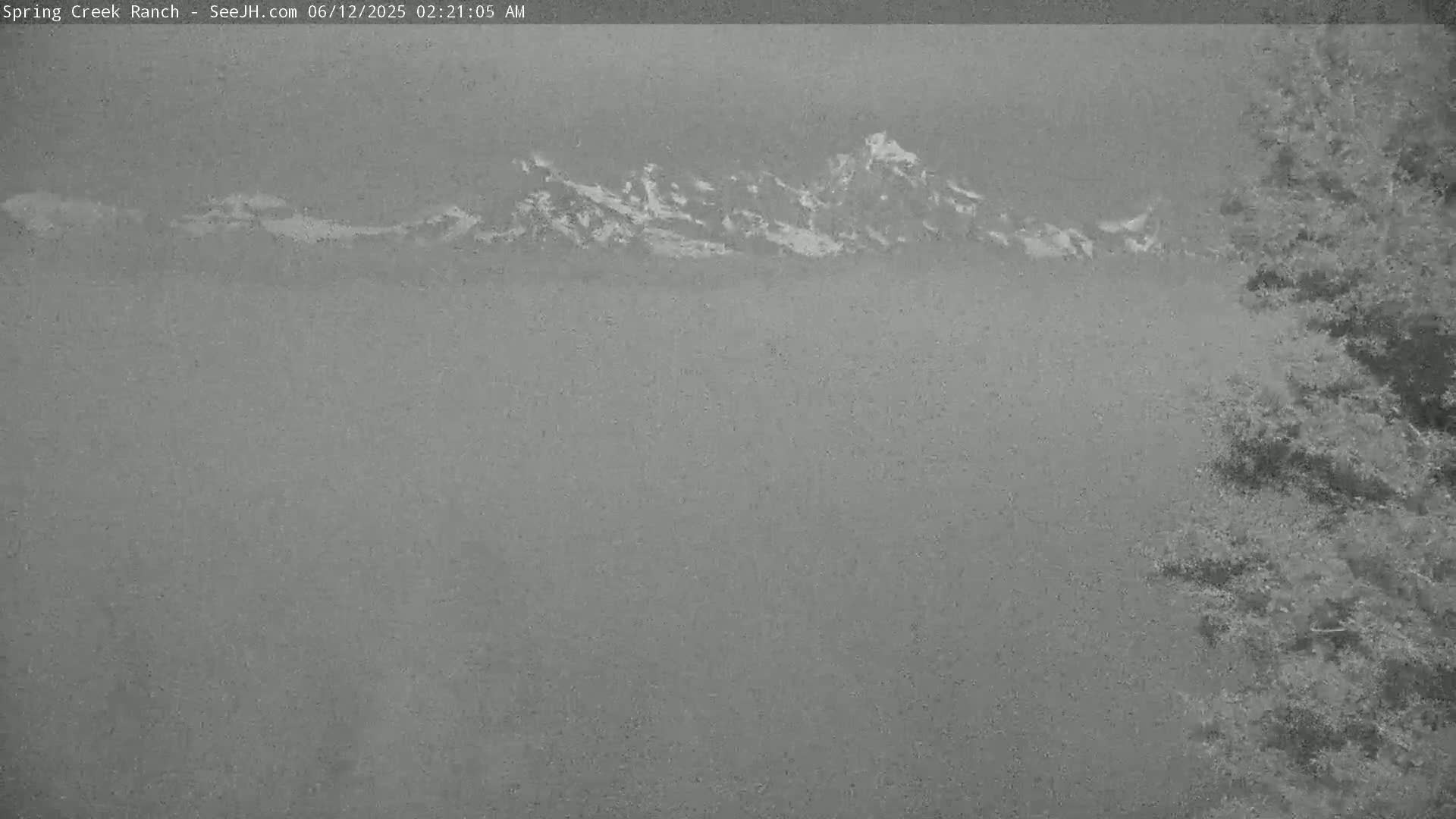 A hazy, overcast view shows distant mountains partially obscured by fog or mist, with some vegetation visible in the lower right corner.