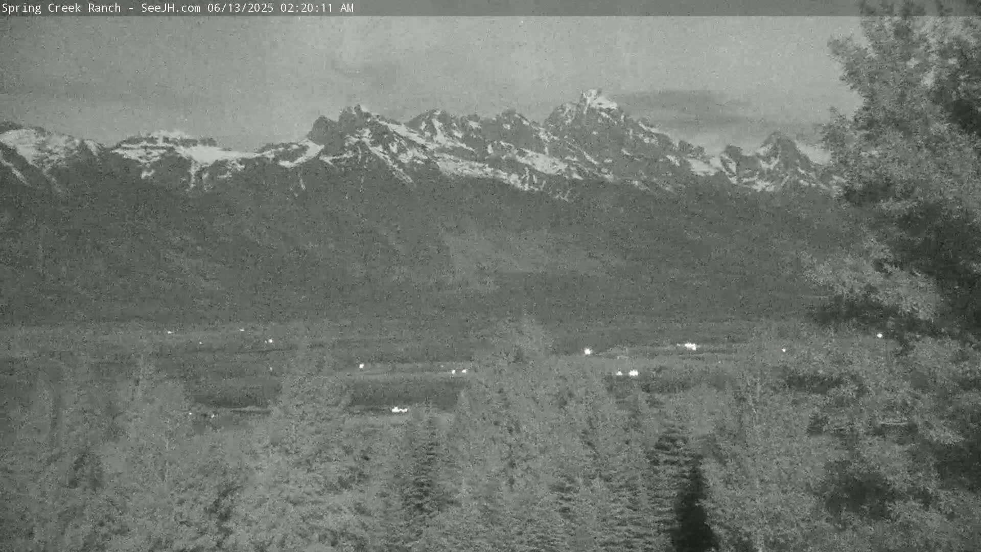 A long shot of snow-capped mountains at dawn, overlooking a valley with sparse lights and trees.