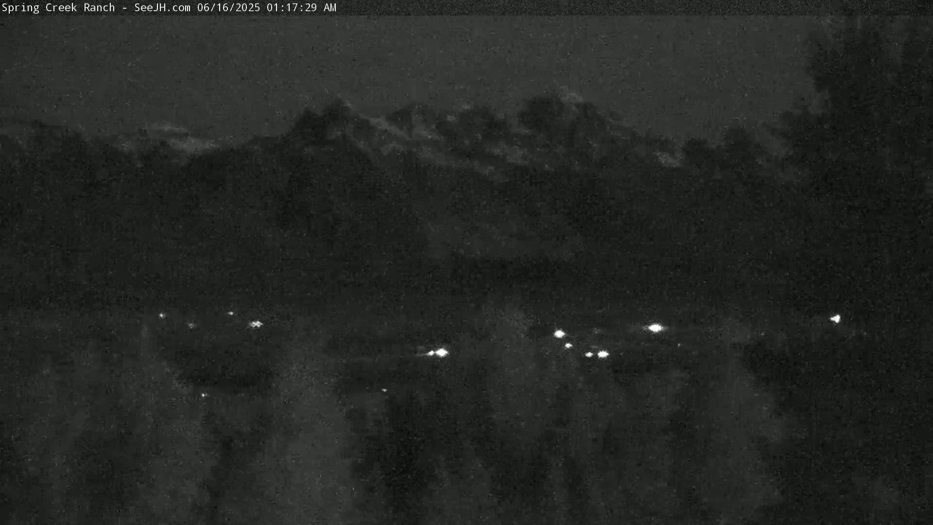 A nighttime, low-light view shows a distant mountain range under a dark sky with a few faint lights visible in the foreground.