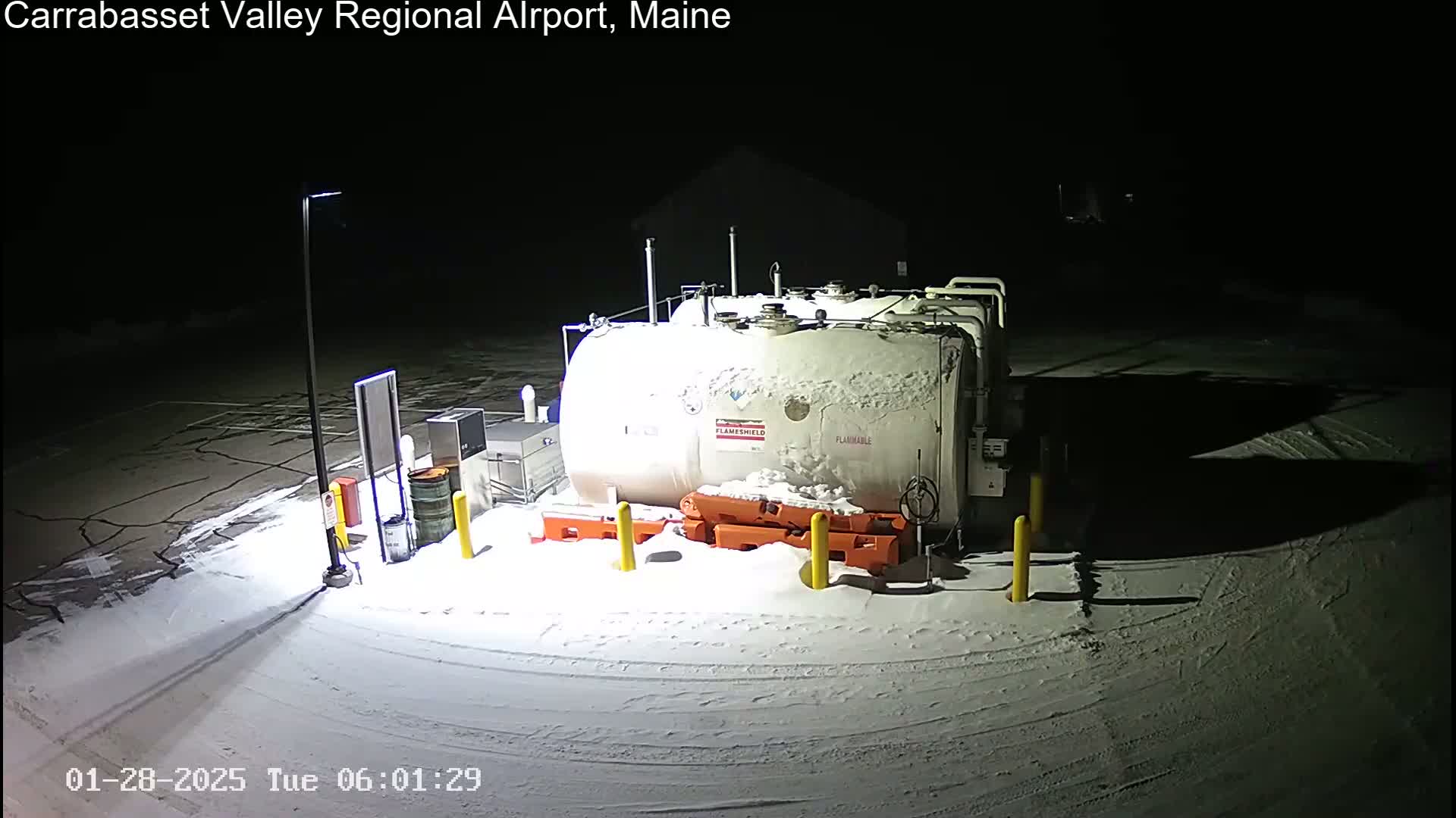 A large, snow-covered fuel tank sits in a snow-covered parking lot at night, illuminated by artificial light.