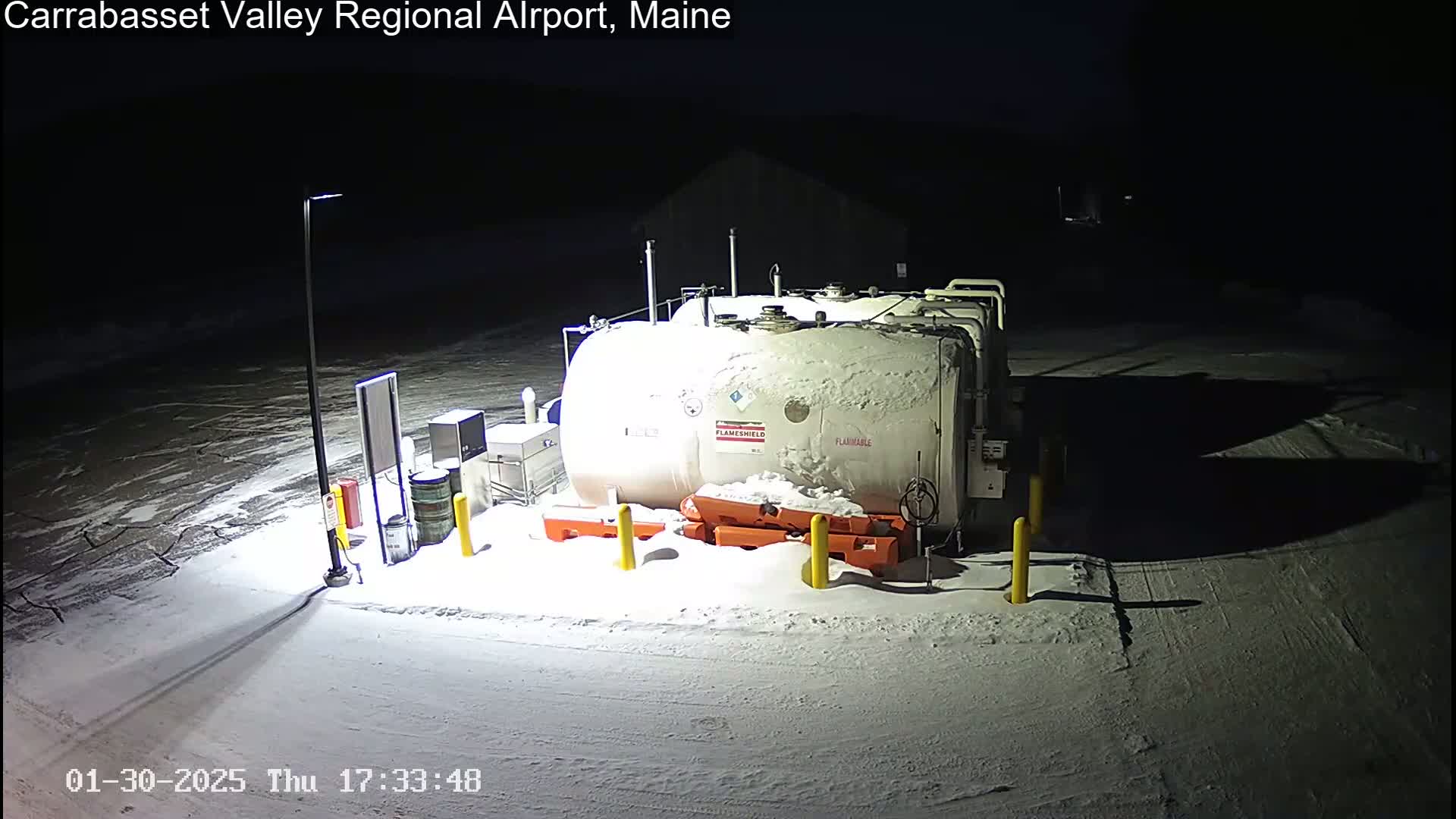 A large, snow-covered fuel tank sits in a snowy, dimly lit outdoor area at night.