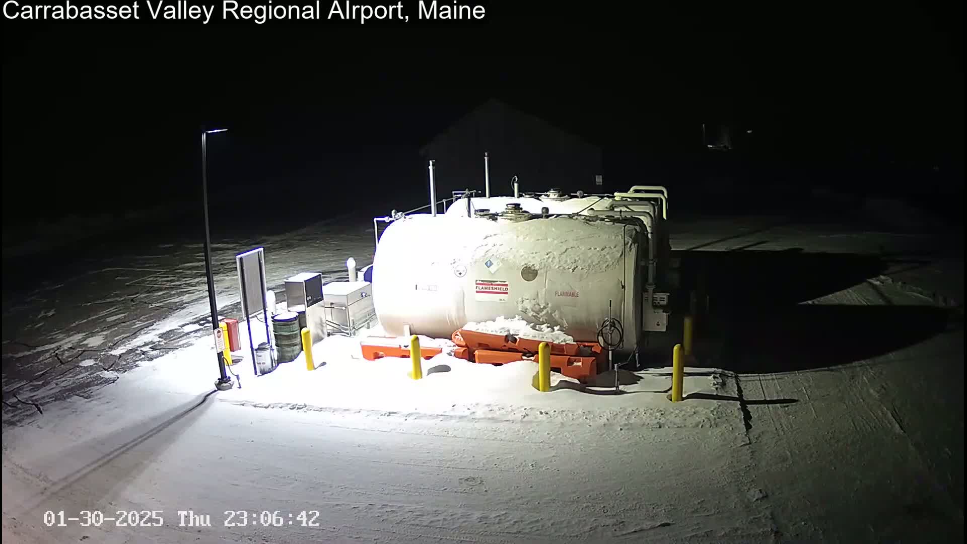 A snow-covered fuel tank and surrounding equipment are illuminated at night.