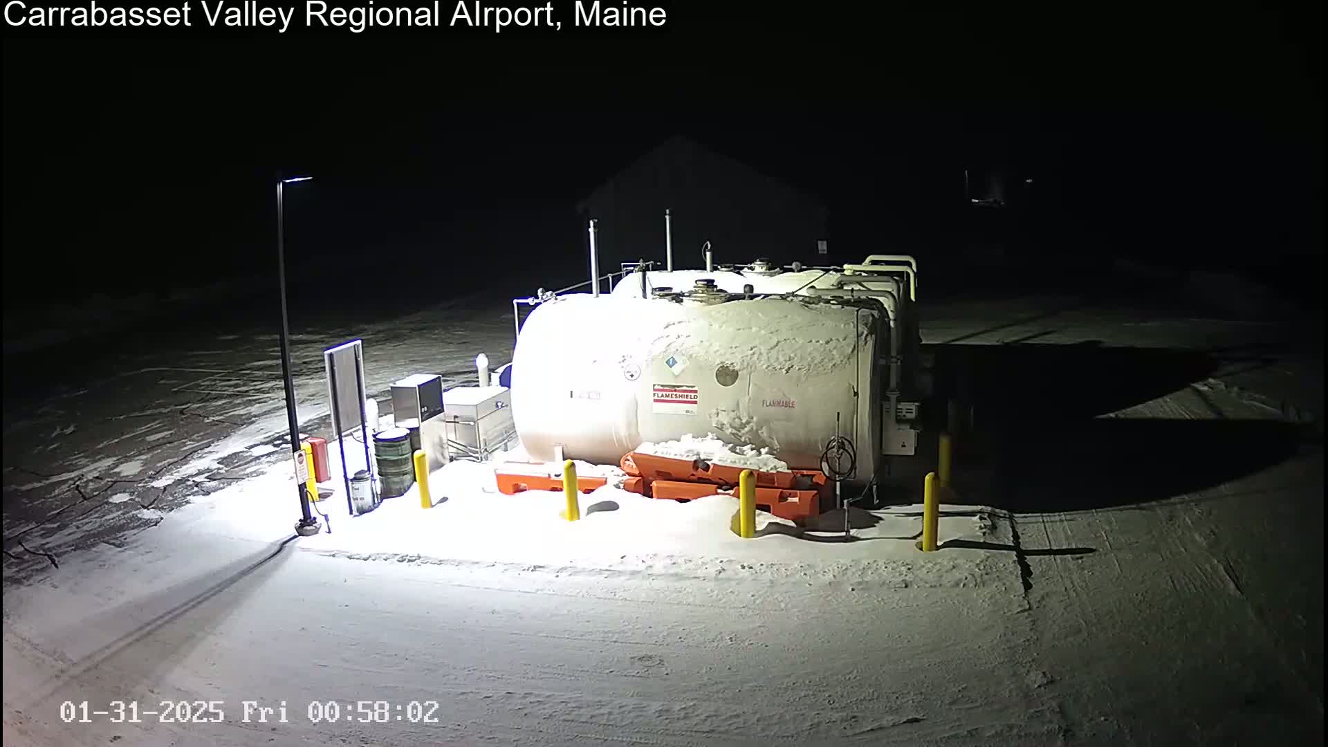 A large, snow-covered fuel tank sits in a snowy, nighttime airfield.