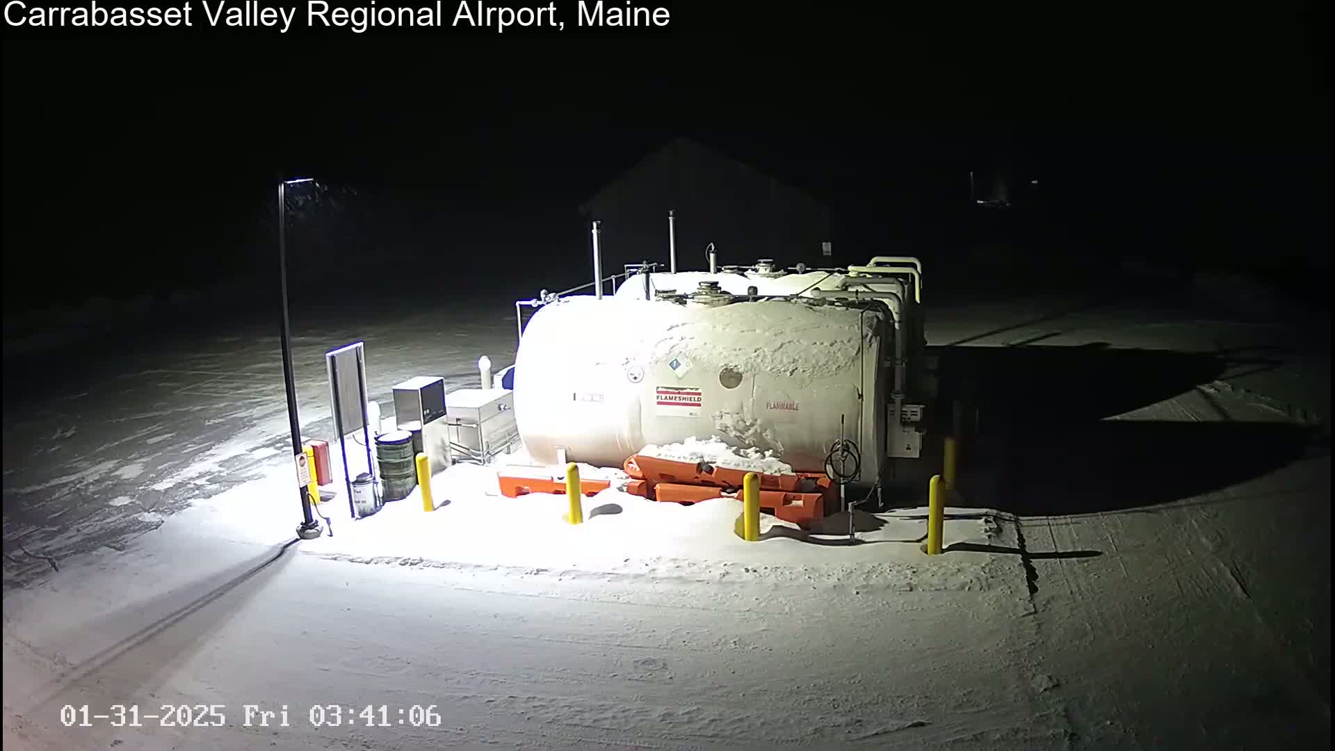 At night, under a snowy cover, a large, cylindrical fuel tank sits in a snow-covered area, illuminated by artificial light.