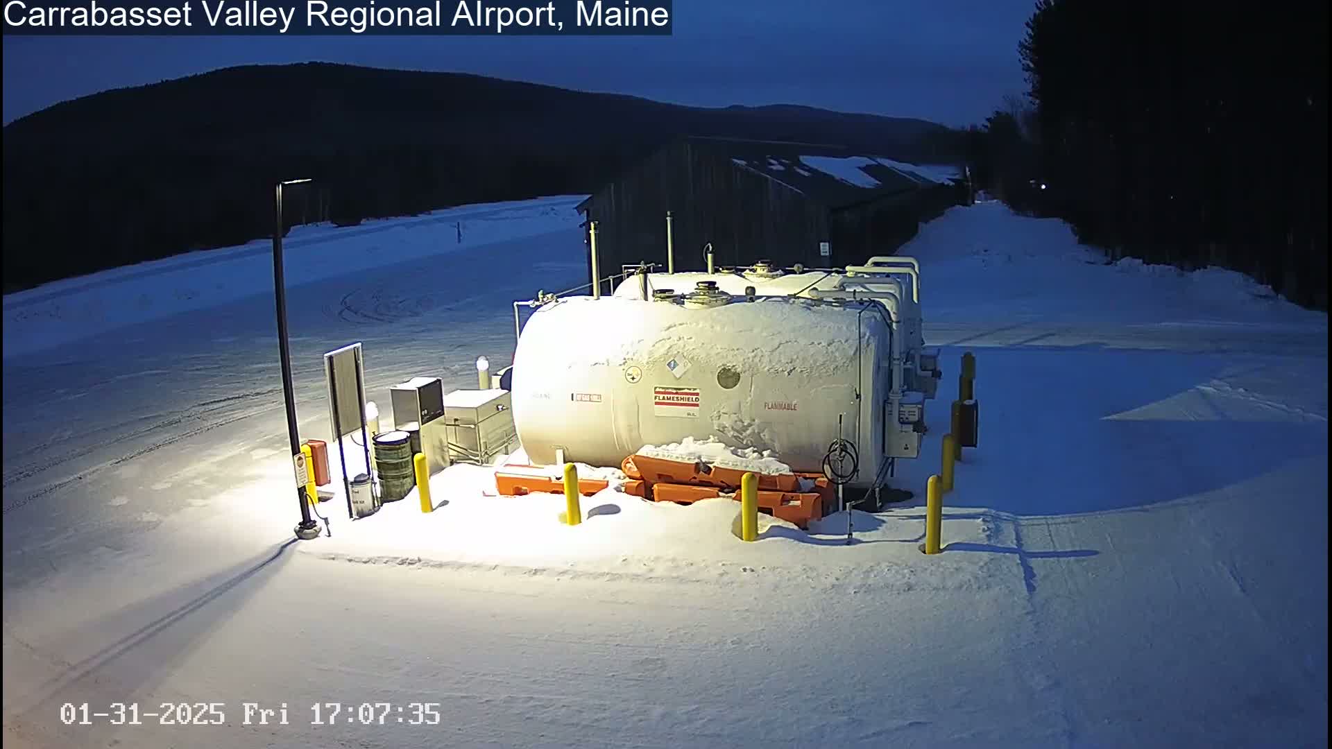 A snow-covered fuel tank sits in a snowy, dimly lit area at night, with a dark mountain in the background.