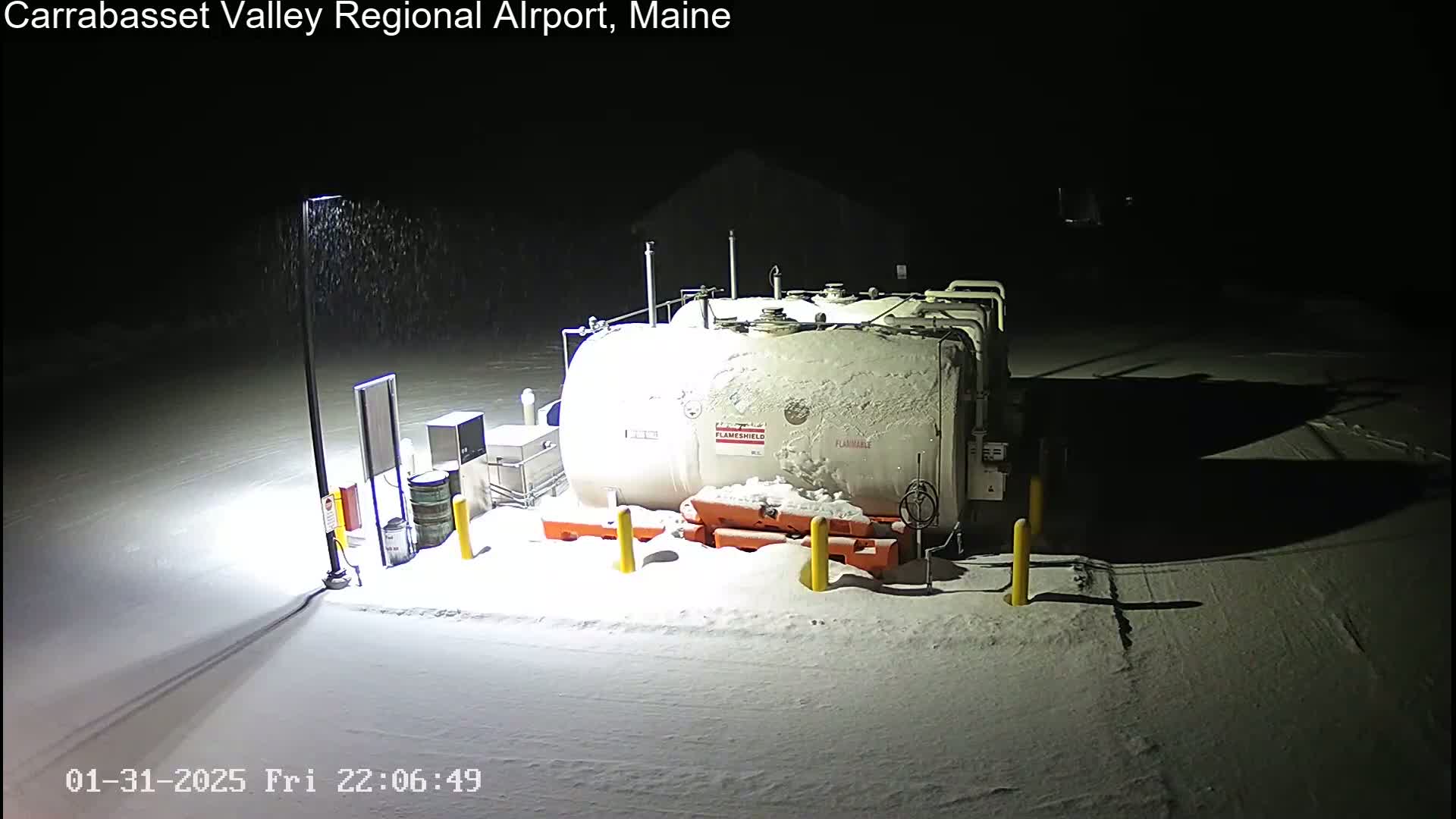 A large, snow-covered fuel tank sits in a snow-covered area at night under light snowfall.