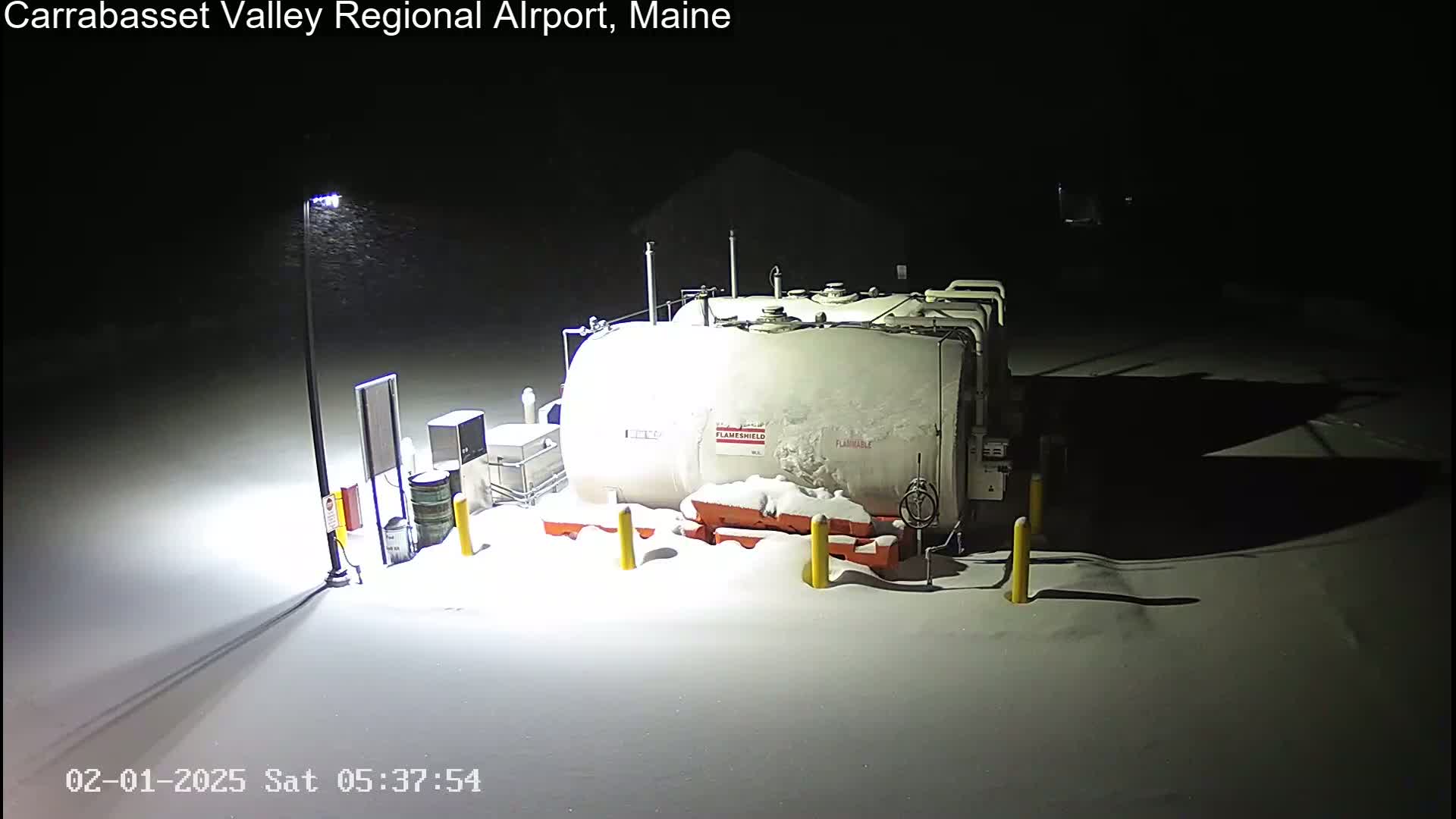 A large, snow-covered fuel tank sits in a snow-covered area at night under a falling snow.