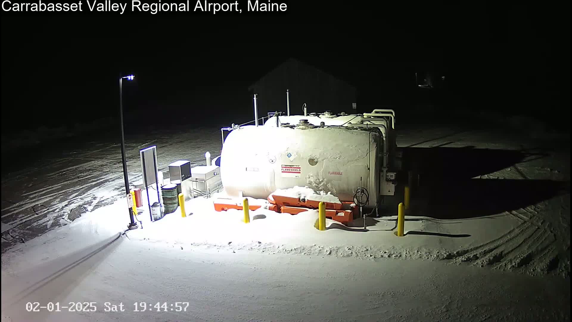 A large, snow-covered fuel tank sits in a snowy, dimly lit area at night.