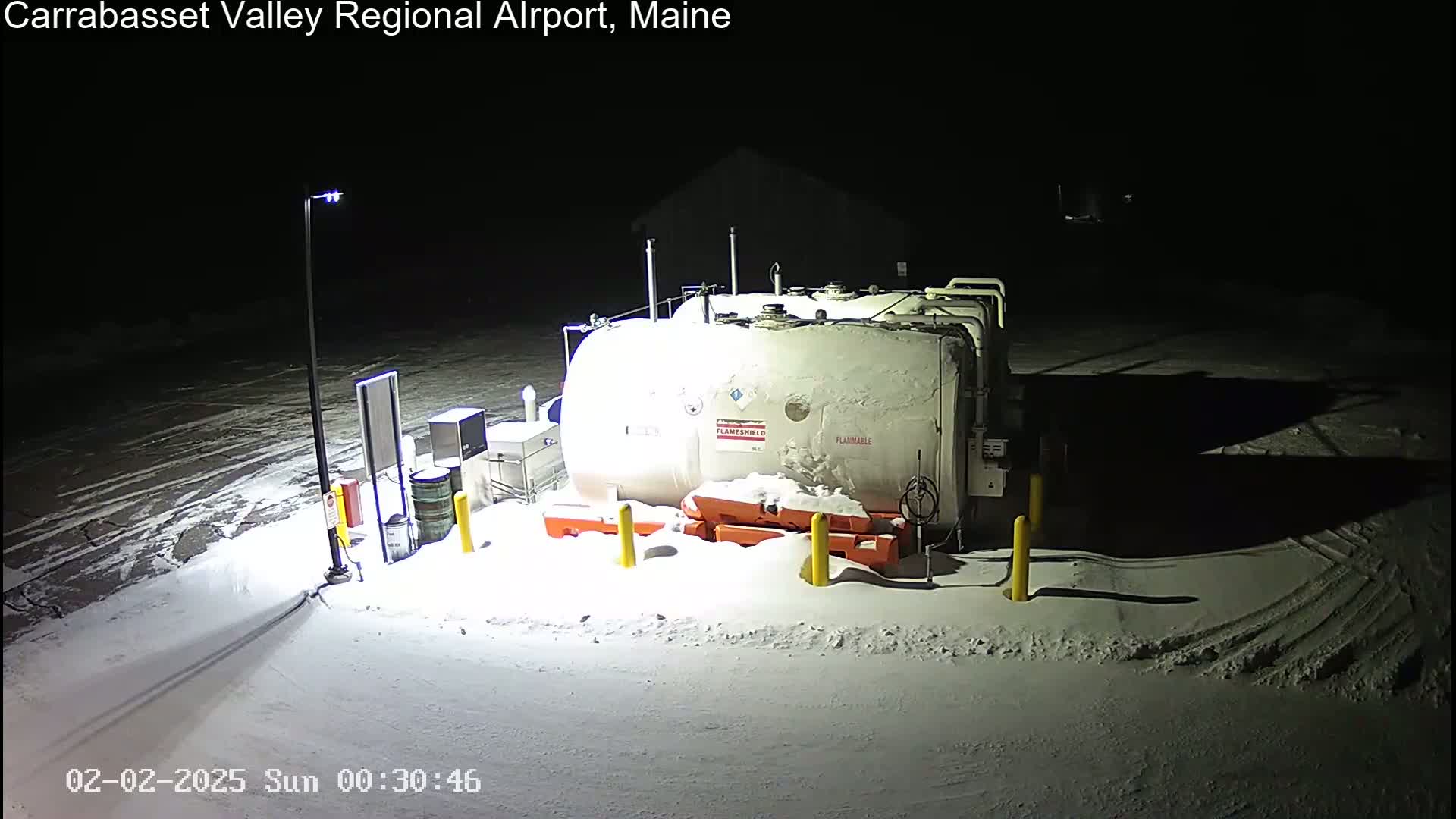 A large, snow-covered fuel tank sits in a snow-covered area at night, illuminated by artificial light.