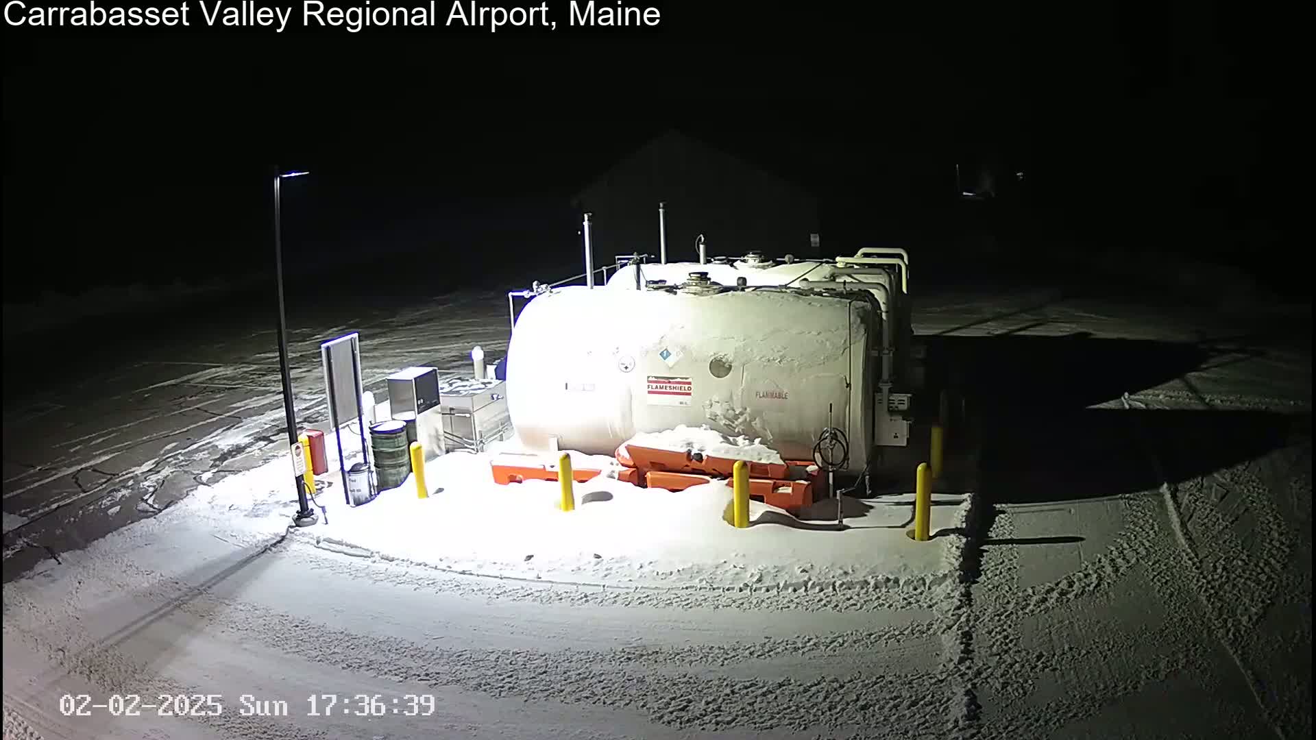 A large, light-colored fuel tank sits in a snow-covered area at night, illuminated by artificial light.