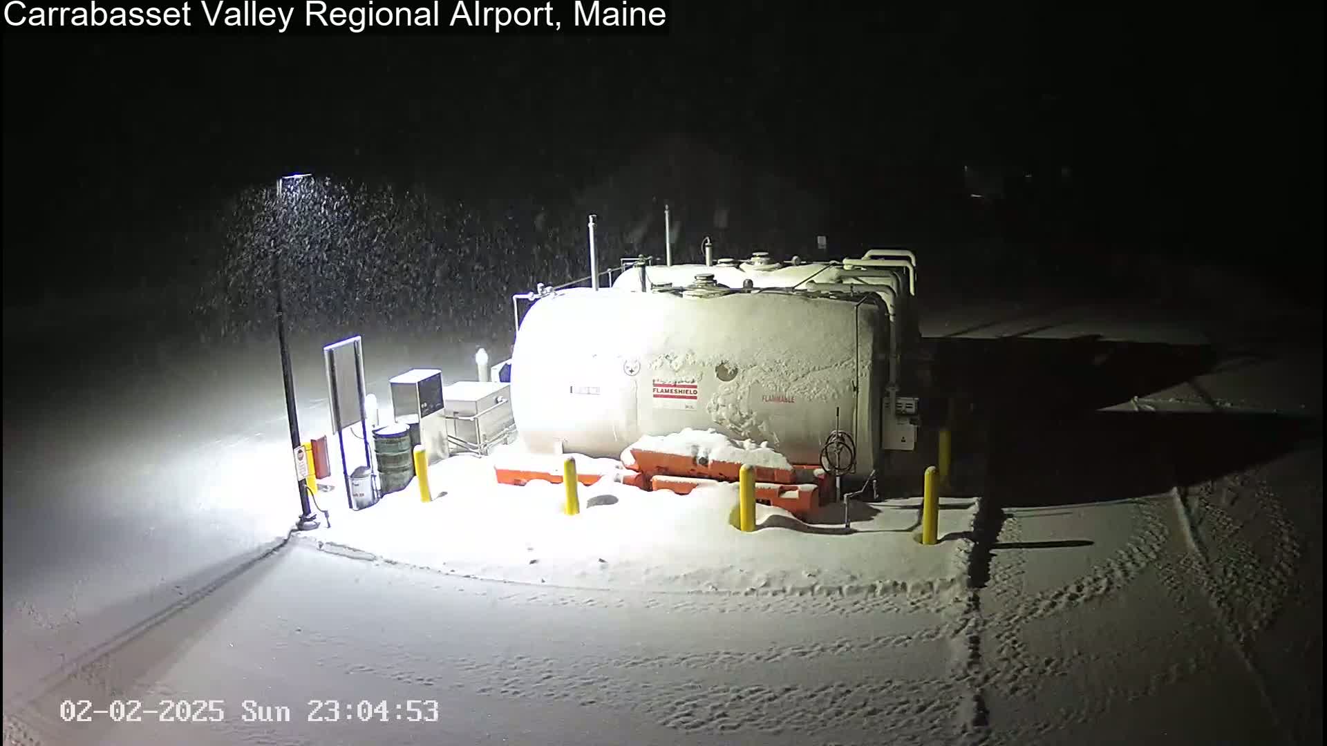 A large, snow-covered fuel tank sits in a snow-covered area at night during a snowfall.