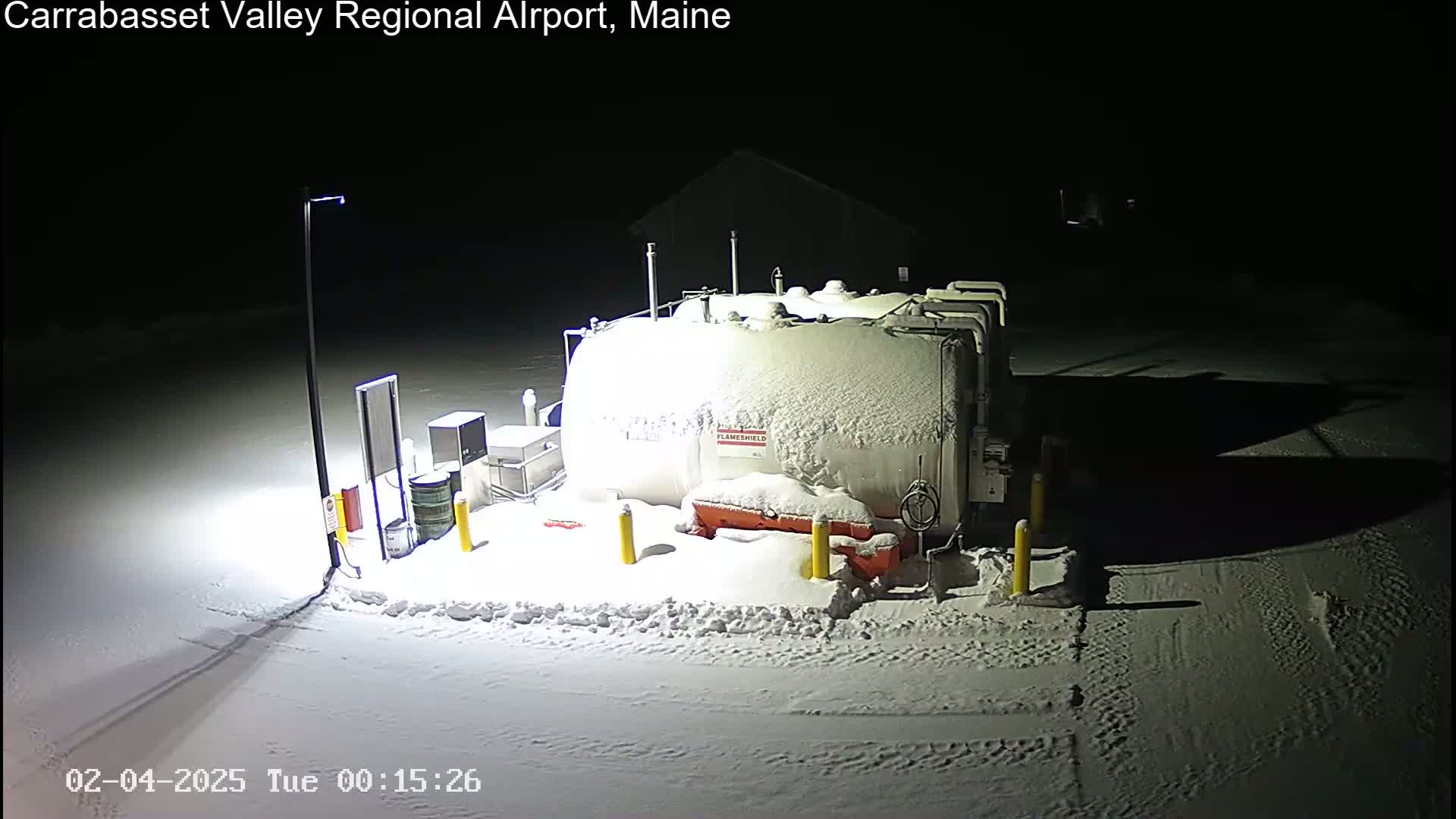 A snow-covered fuel tank and surrounding equipment are illuminated at night in a snowy landscape.