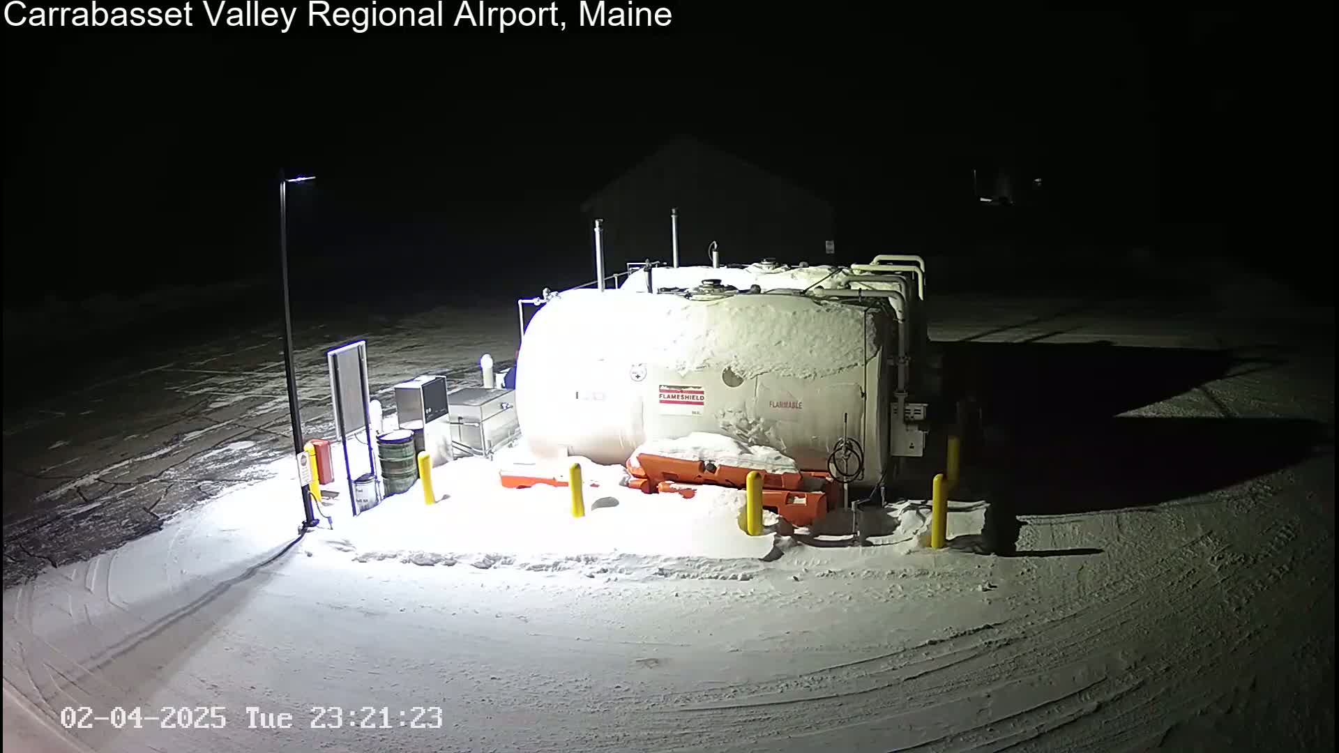 A large, snow-covered fuel tank sits in a snow-covered parking lot at night.