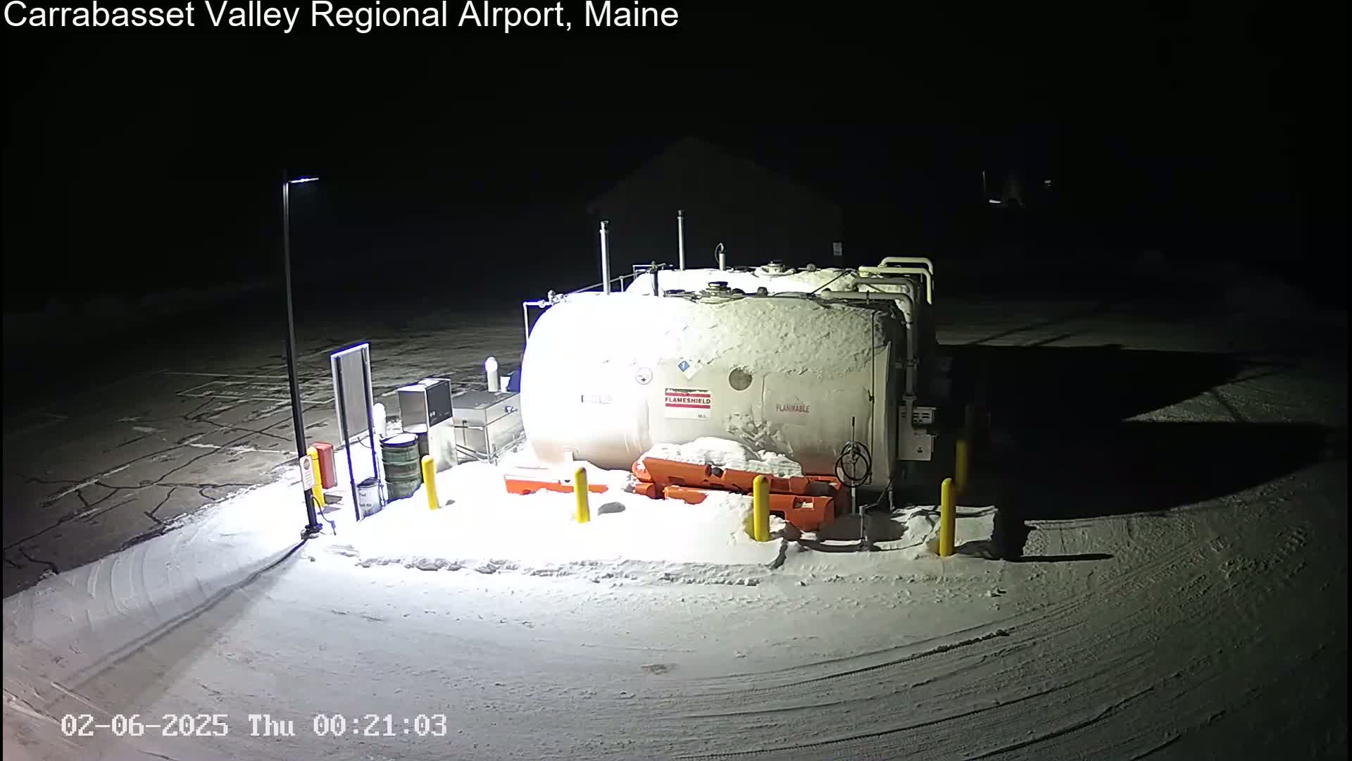 A large, snow-covered fuel tank sits in a snow-covered parking lot at night.