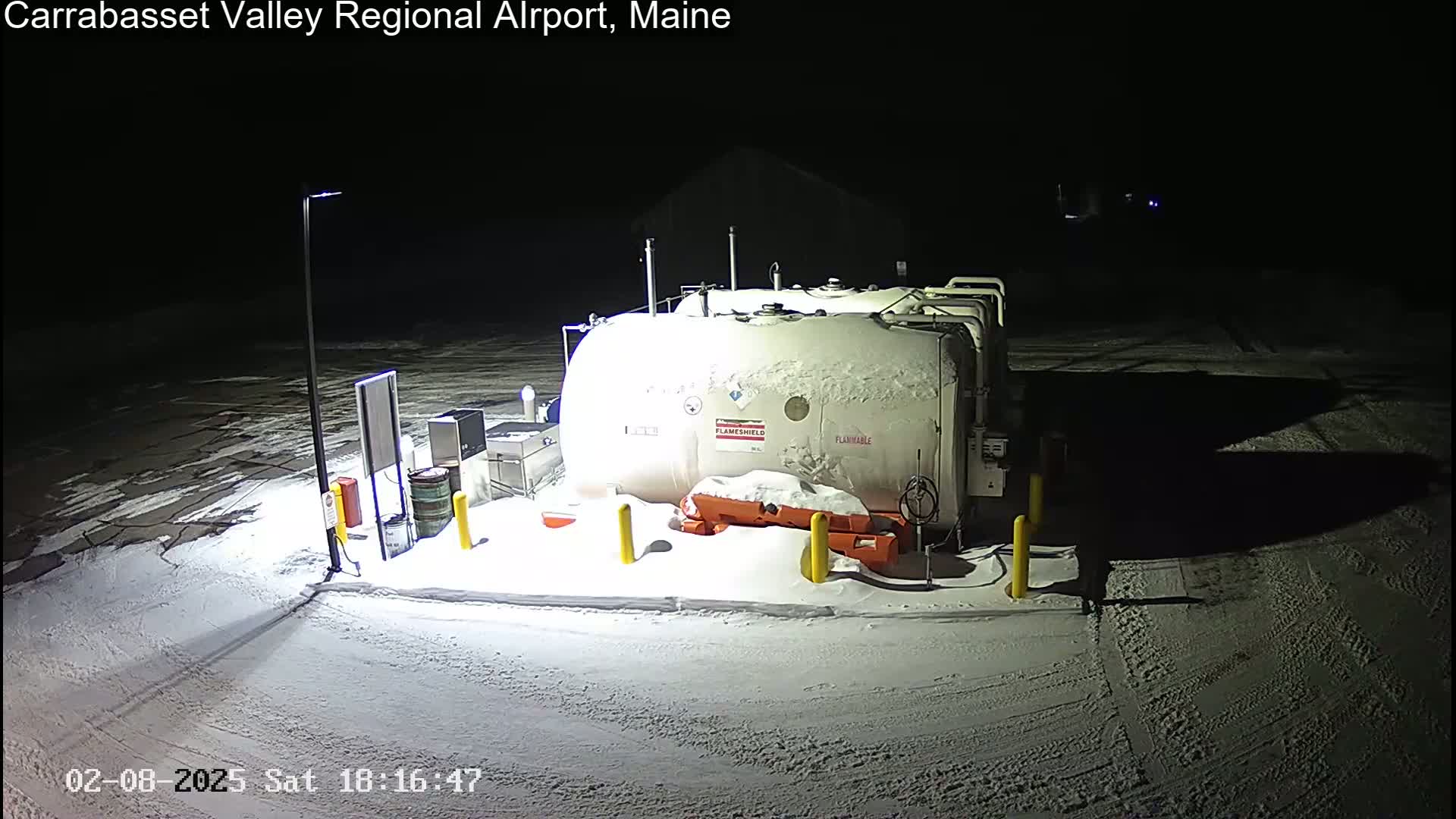 A snow-covered fuel tank sits in a snowy, nighttime airport lot.