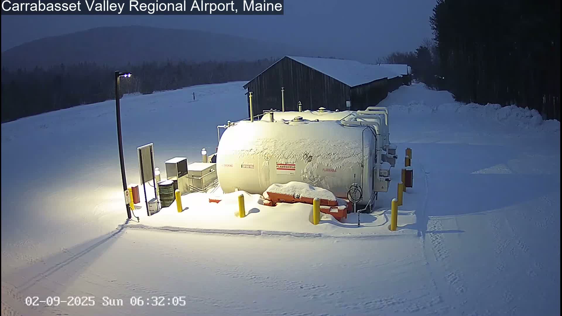 A snow-covered fuel tank and surrounding equipment are visible at night in a snowy, outdoor setting.