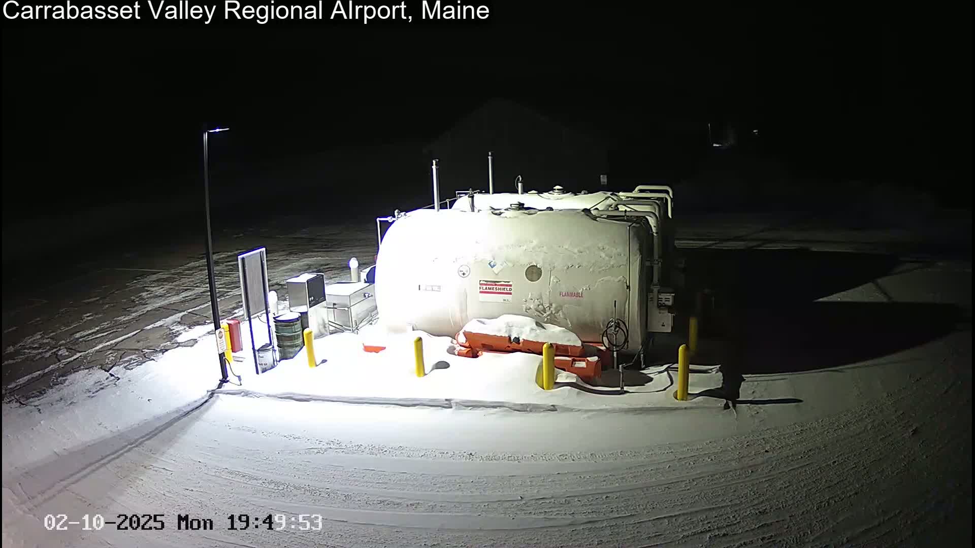A snow-covered fuel storage tank and surrounding equipment are illuminated at night.