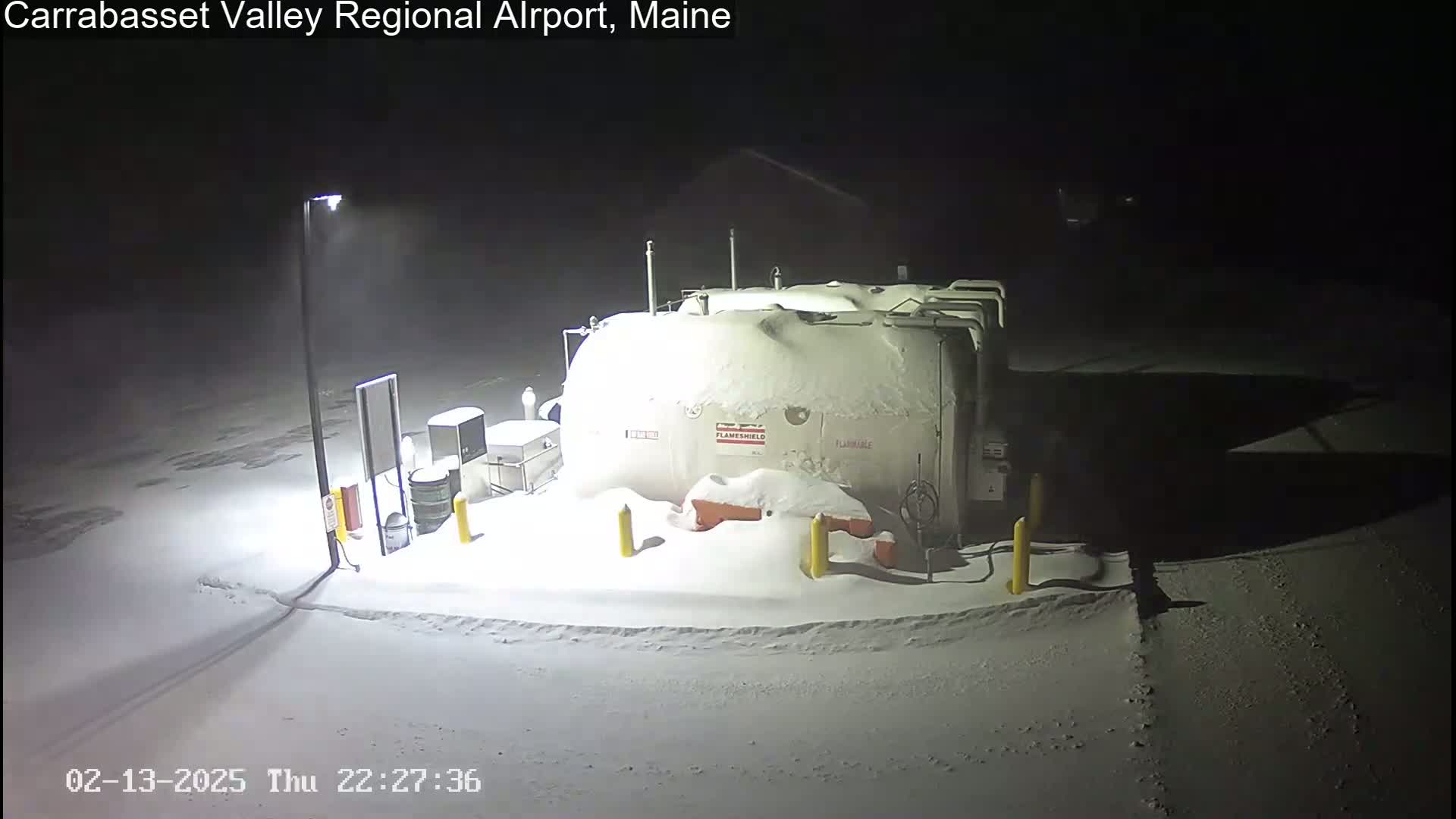 A large, snow-covered fuel tank and surrounding equipment are illuminated at night in a heavy snowfall.