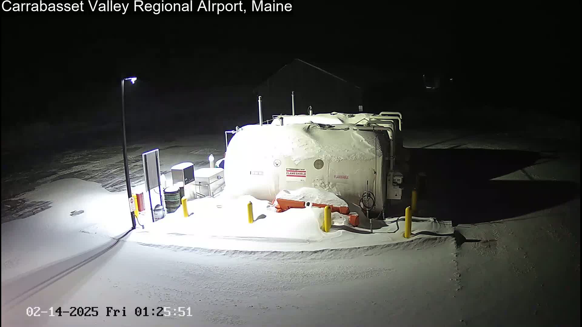A snow-covered fuel tank and surrounding equipment are illuminated at night.