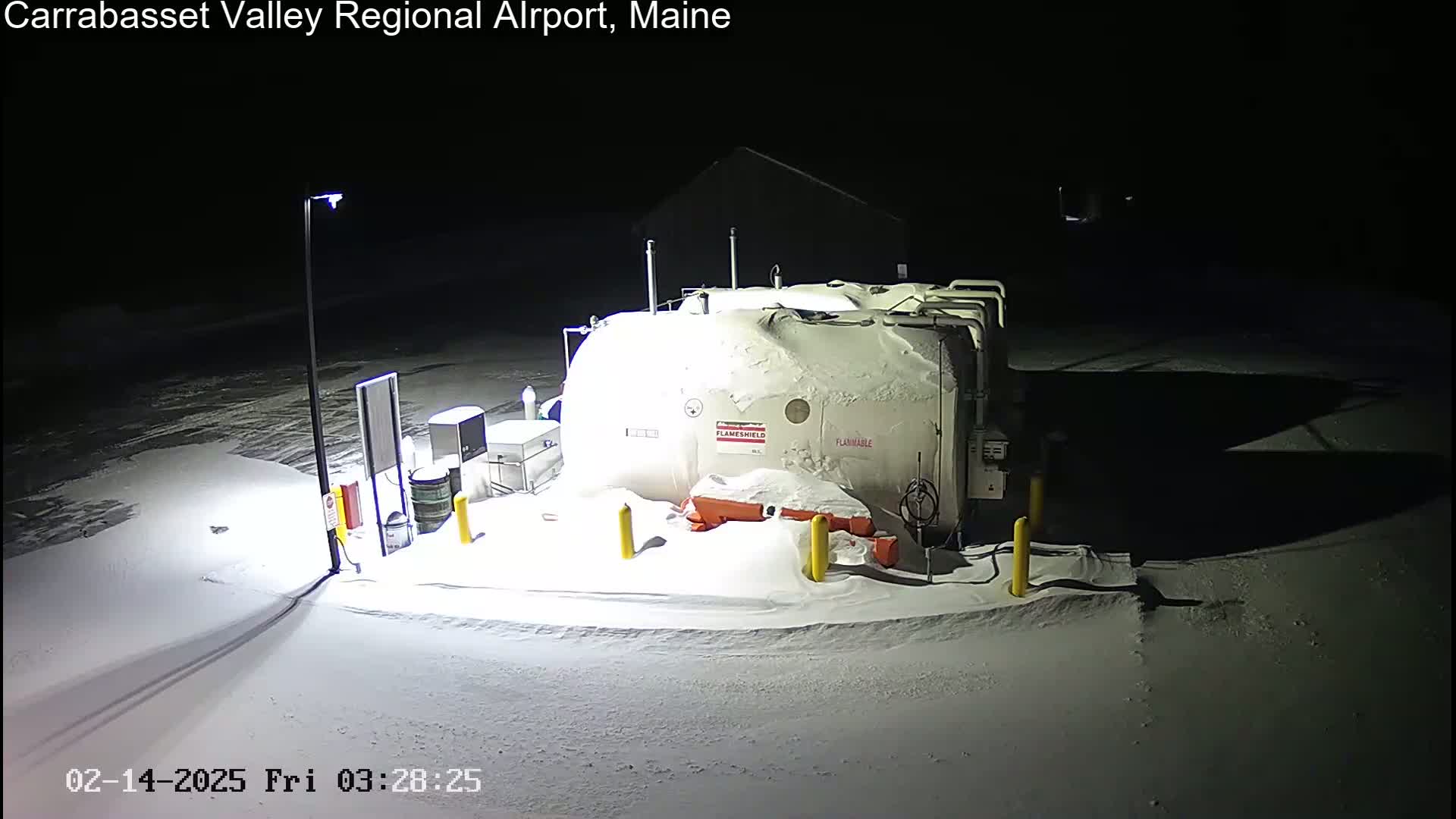 A large, snow-covered fuel tank and associated equipment are illuminated at night in a snowy area.