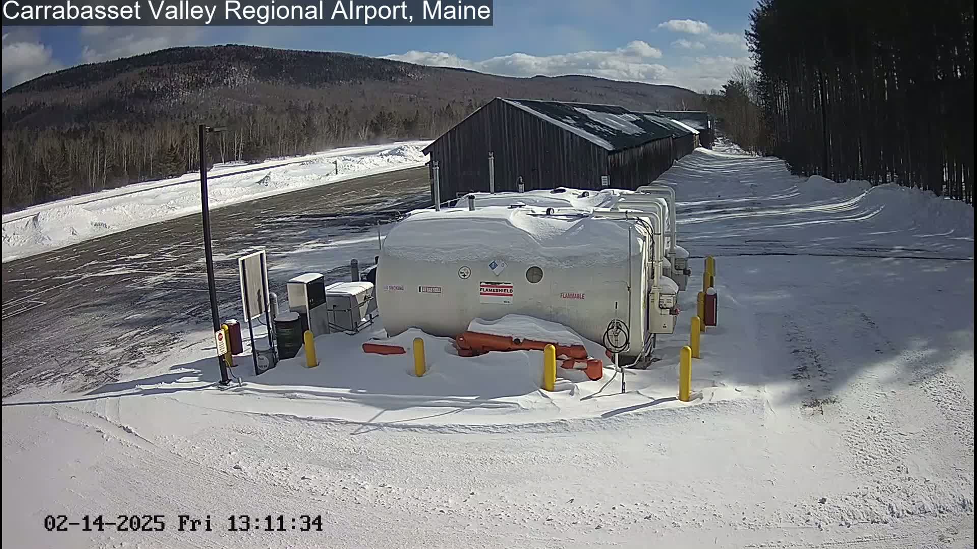Snow-covered fuel tanks sit near a long, snow-covered building under a sunny sky.