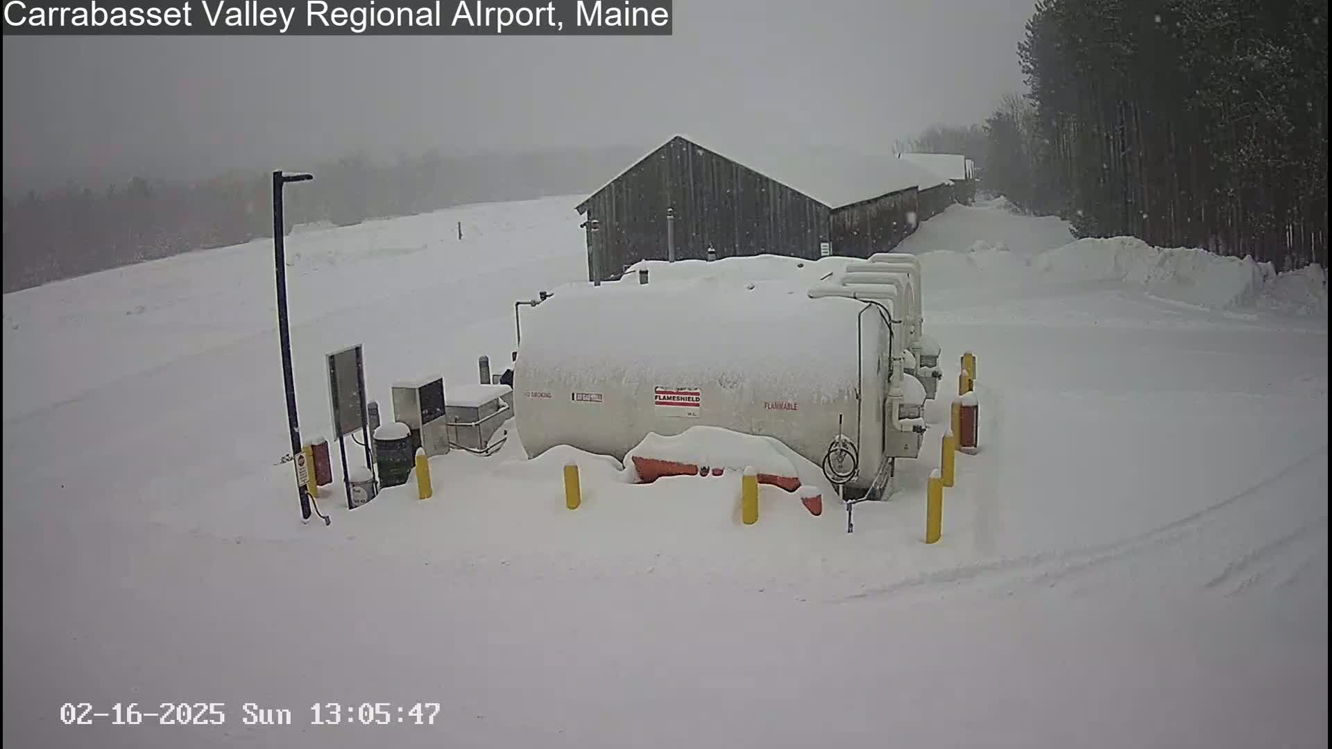 A snow-covered fuel tank farm is situated near a snow-covered building in a heavy snowfall.