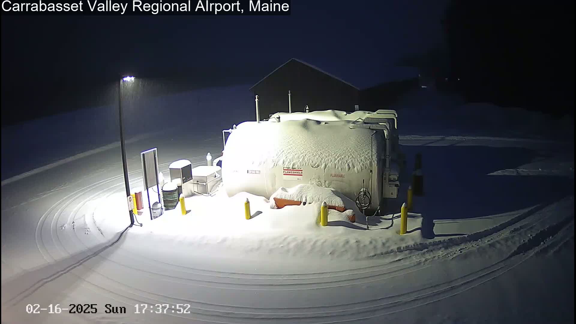 A large, snow-covered fuel tank sits in a snow-covered area at night, under light snowfall.
