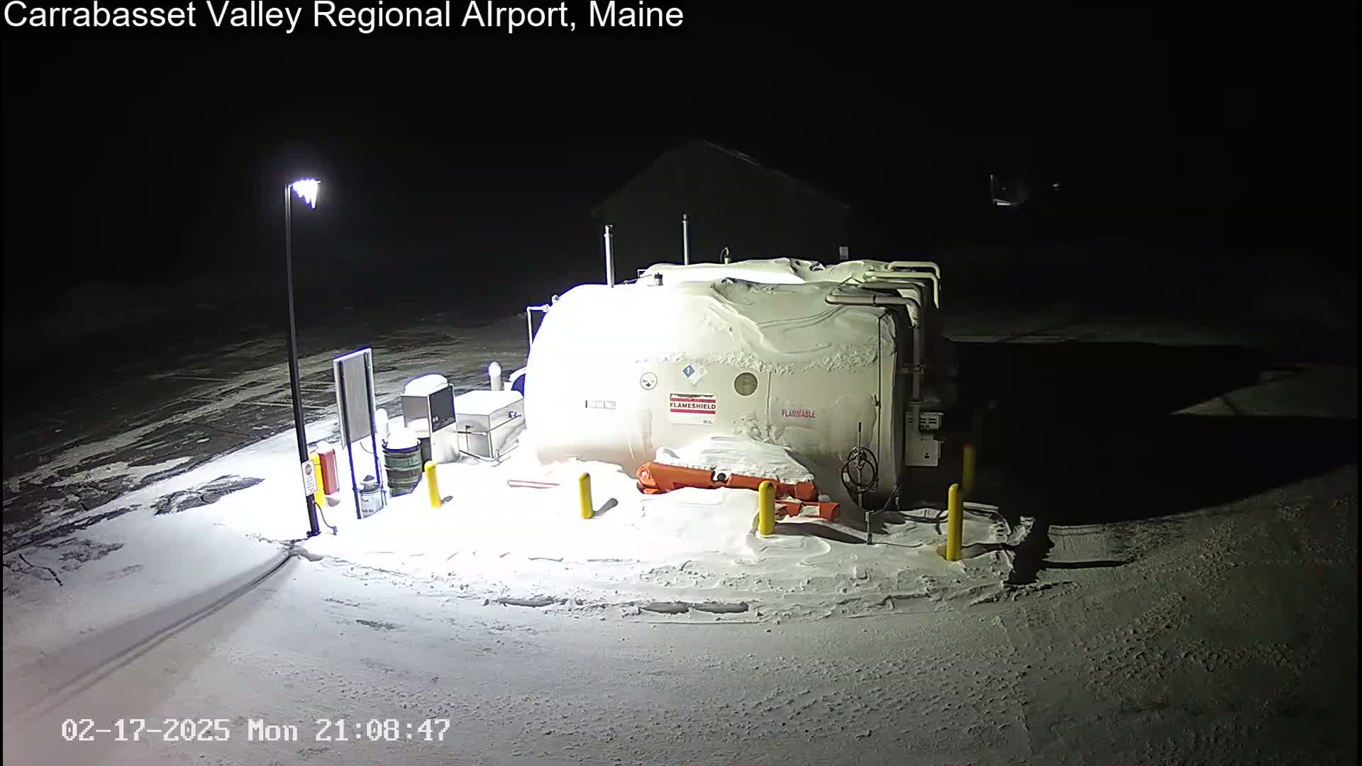 A snow-covered fuel tank and surrounding area are illuminated at night by a single lamppost.