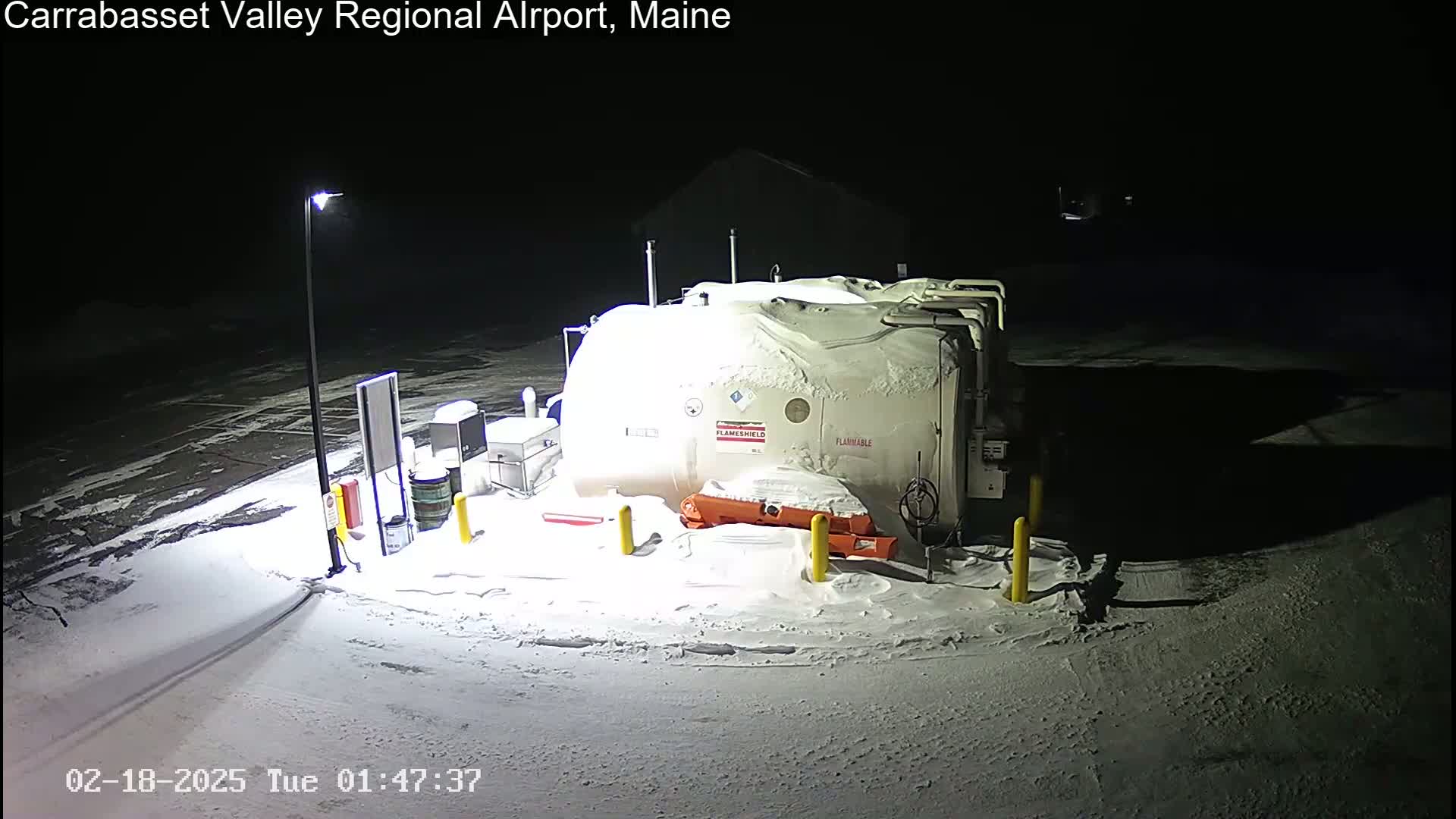 A snow-covered fuel tank and surrounding equipment are illuminated at night.