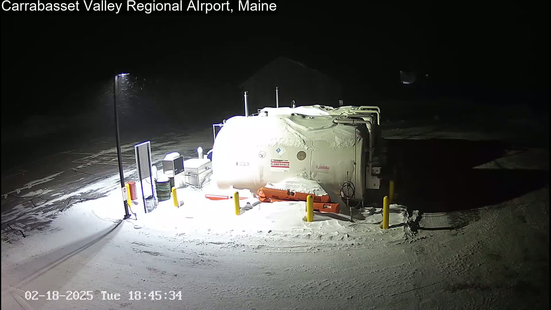 A large, snow-covered fuel tank sits in a snow-covered parking lot at night.