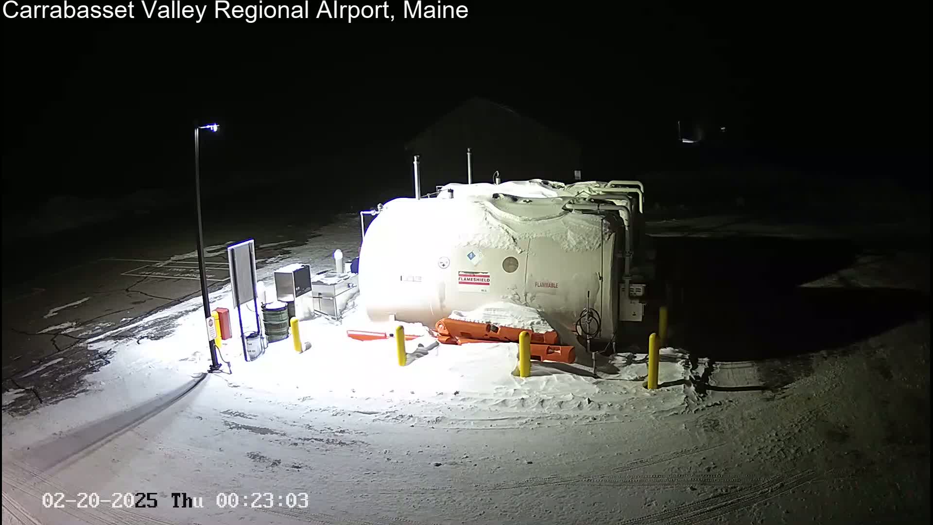 A large, snow-covered fuel tank sits in a snow-covered parking lot at night.