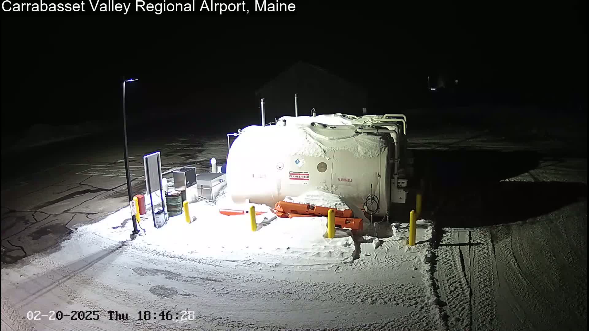 A large, snow-covered fuel tank sits in a snow-covered parking lot at night.