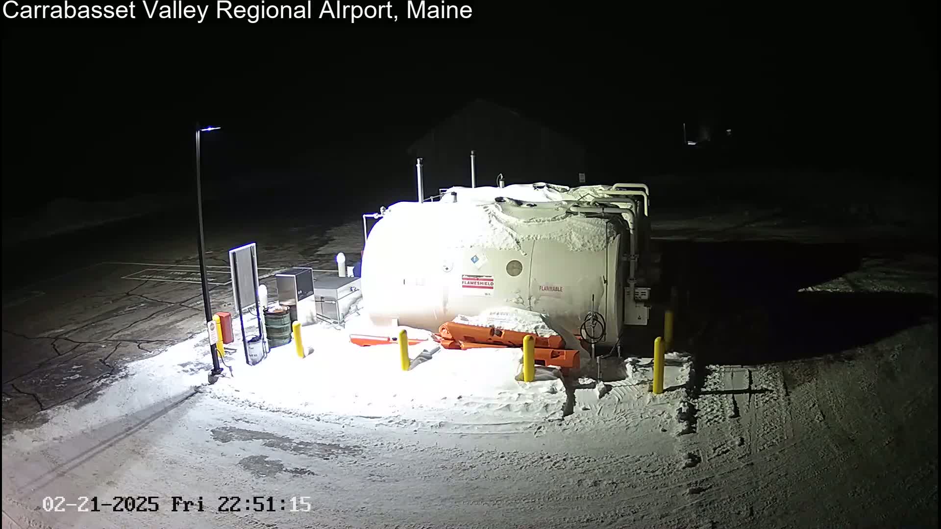 A large, snow-covered fuel tank sits in a snow-covered parking lot at night.