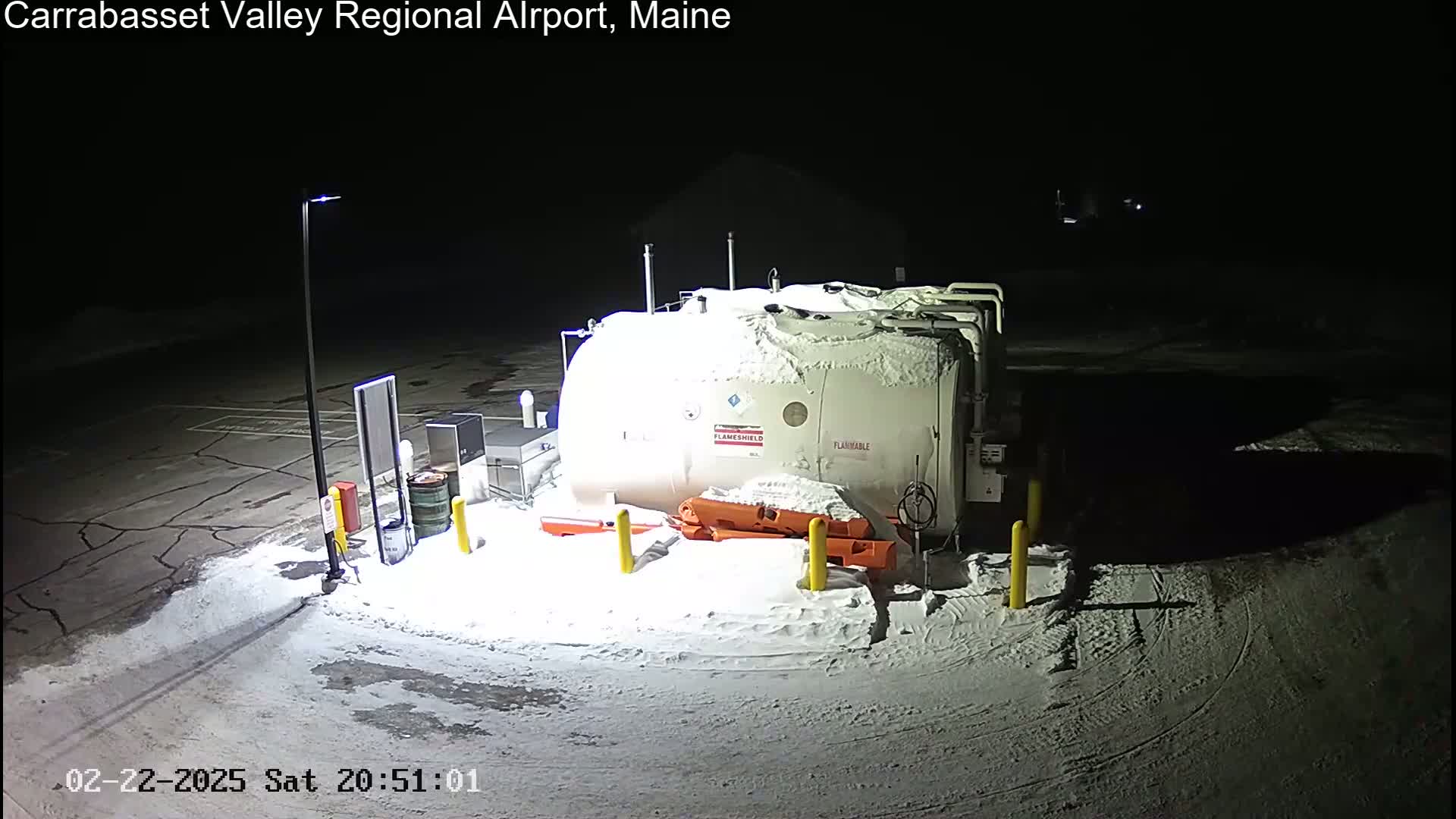 A large, snow-covered fuel tank sits in a snow-covered parking lot at night.