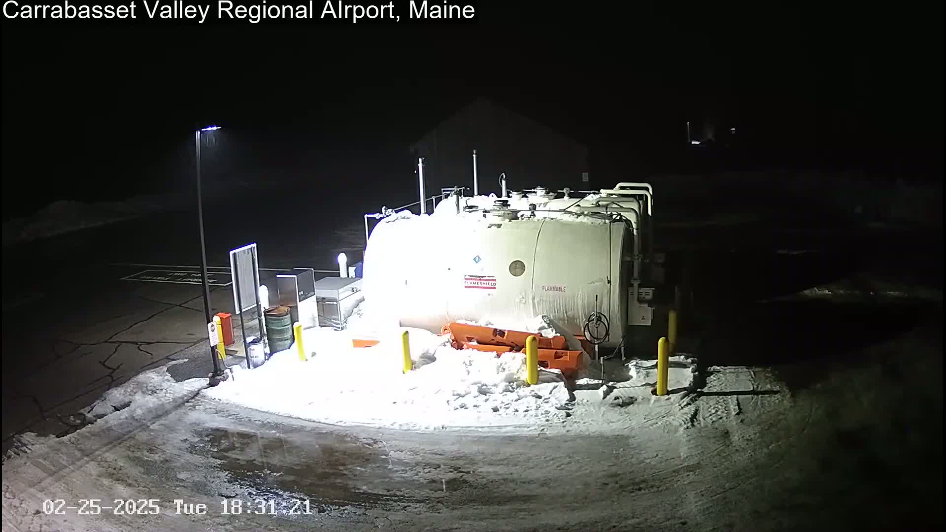 A large, snow-covered fuel tank sits in a snow-covered parking lot at night, illuminated by artificial light.