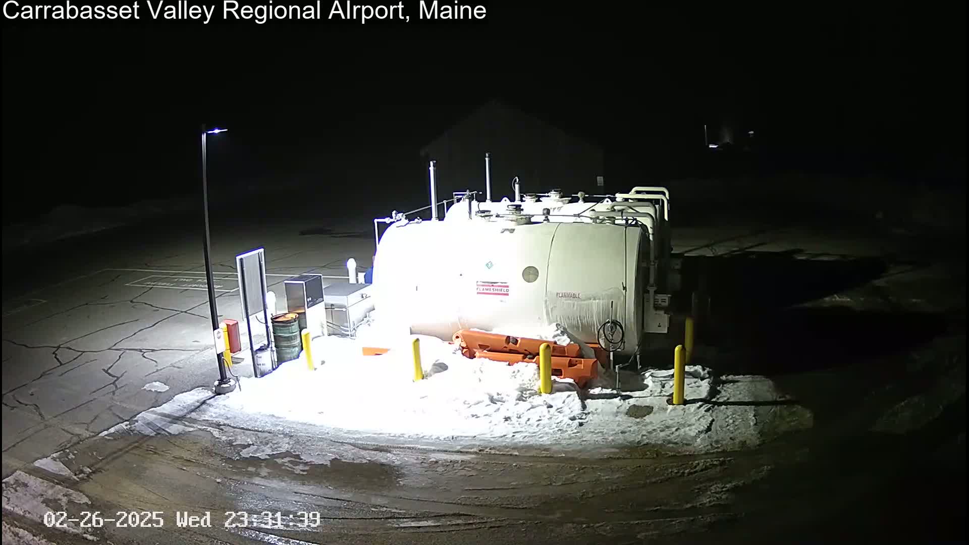 A large white fuel tank sits in a snow-covered area at night, illuminated by artificial lights.